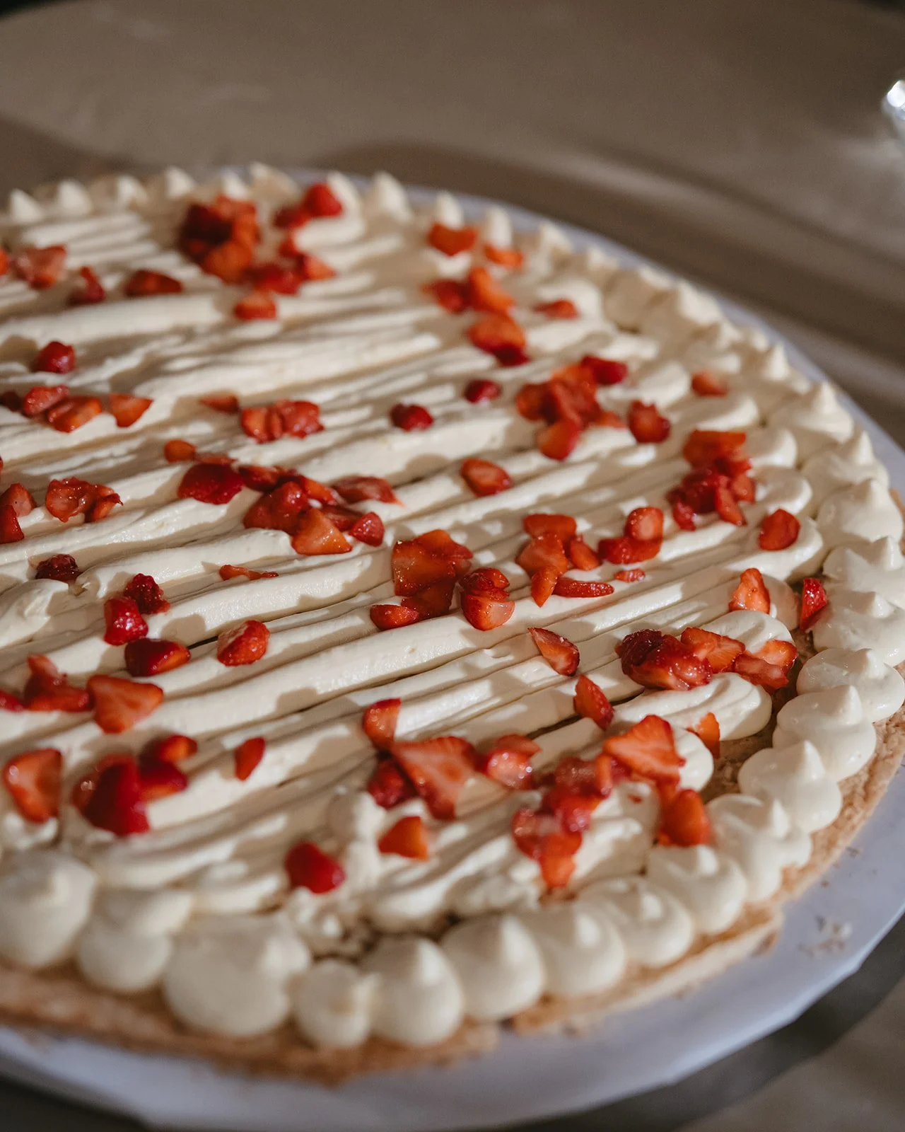 A close-up of a strawberry shortcake with whipped cream and chopped strawberries on top, with a decorated border of whipped cream around the edges.