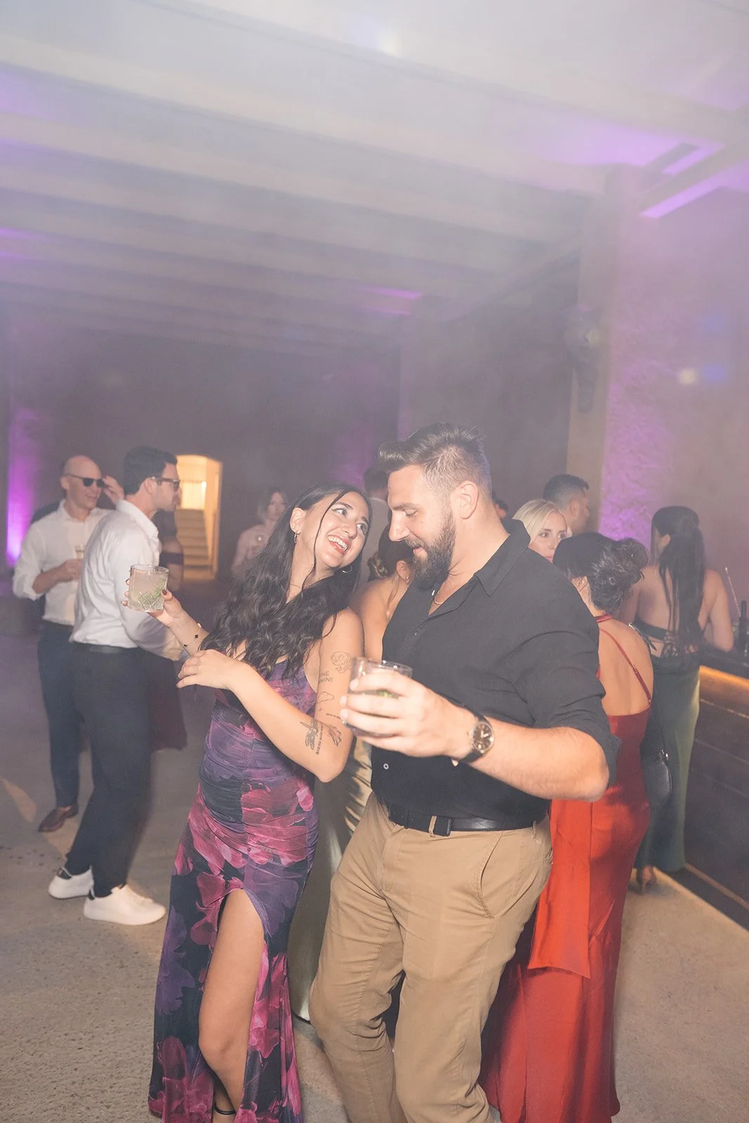 People dancing and socializing at a party in a dimly lit venue with purple lighting.