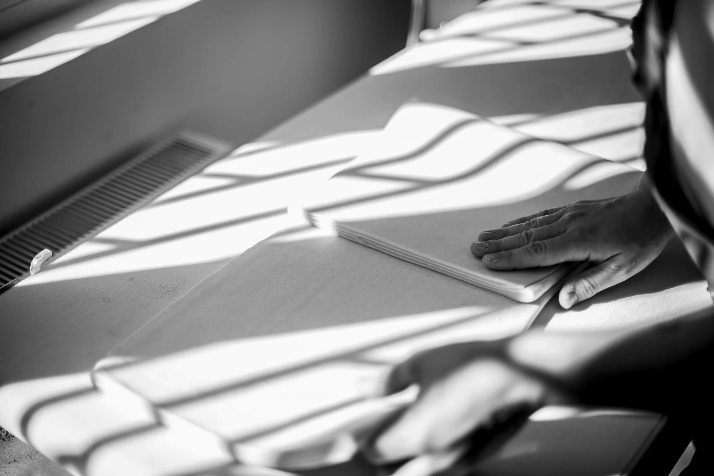 A person's hand resting on folded napkins on a table, with sunlight casting shadows through blinds.