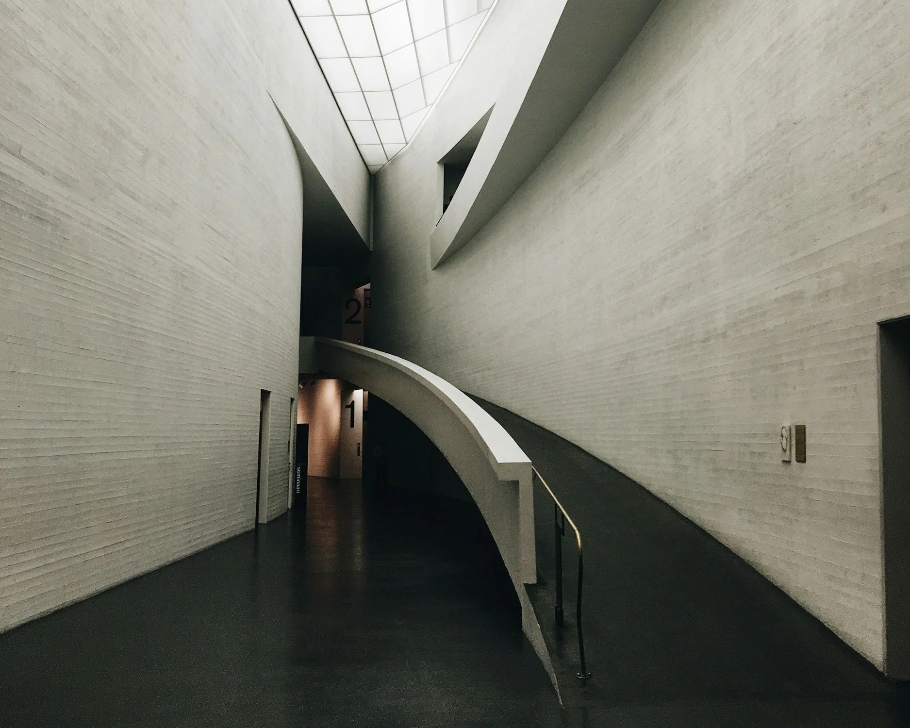 Modern interior building corridor with curved staircase, white walls, and high ceiling with skylight.