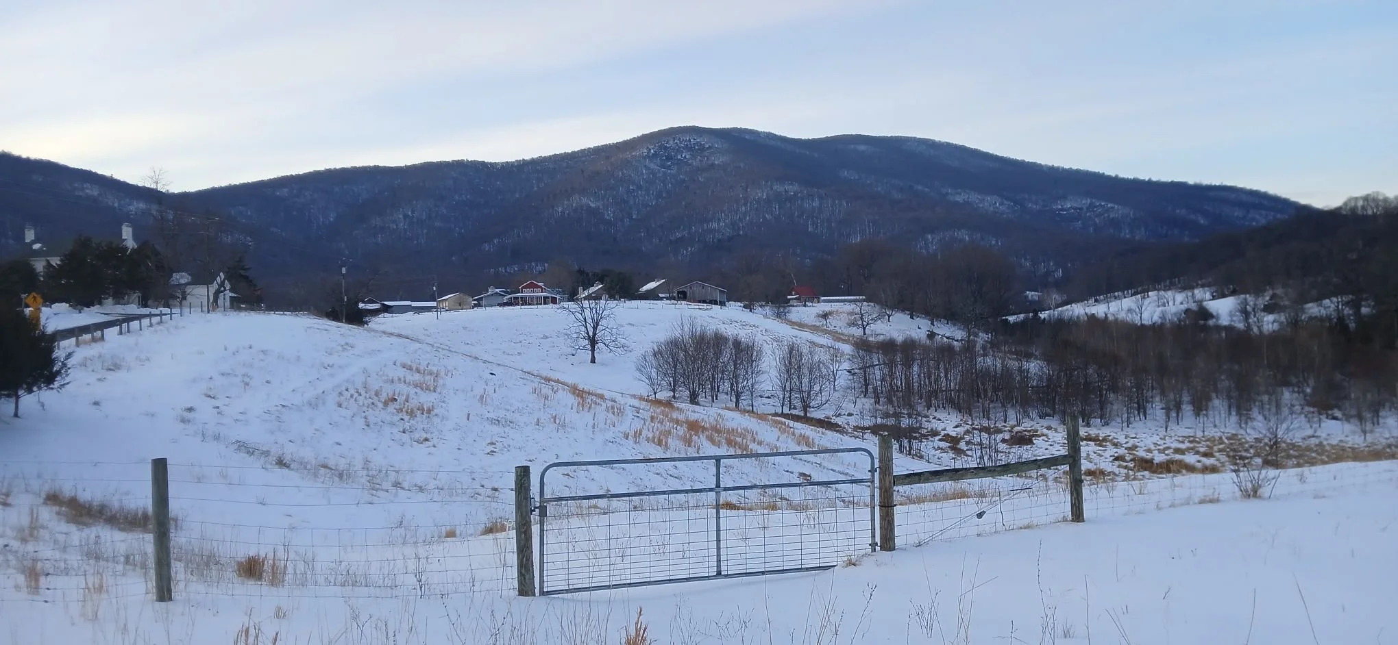snowy mountains at dusk with gate in foreground and farm buildings in background