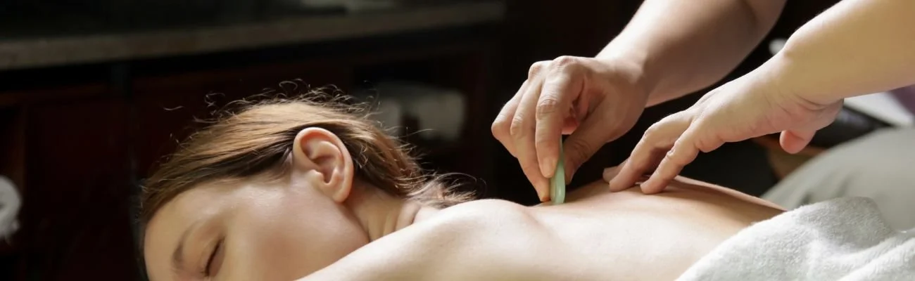 Person receiving a gua sha treatment on their back with a stone tool.