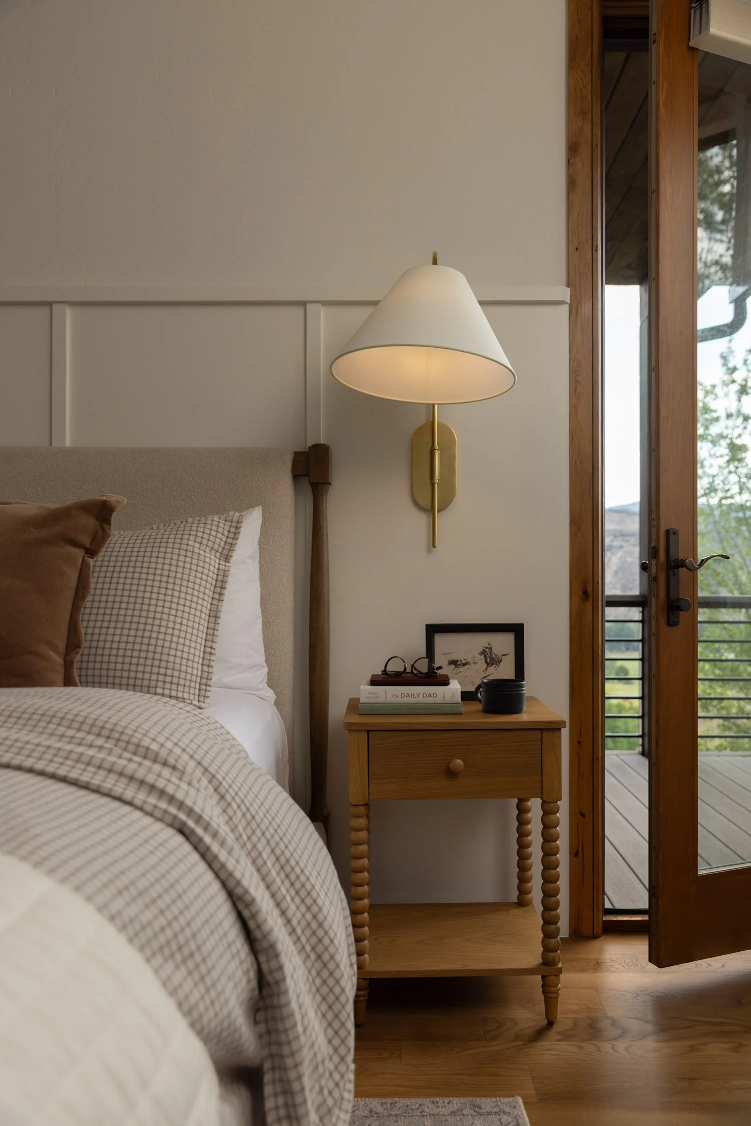 Natural bedroom with wood end table, millwork, and wall sconce in Vail home designed by Krista Weisman
