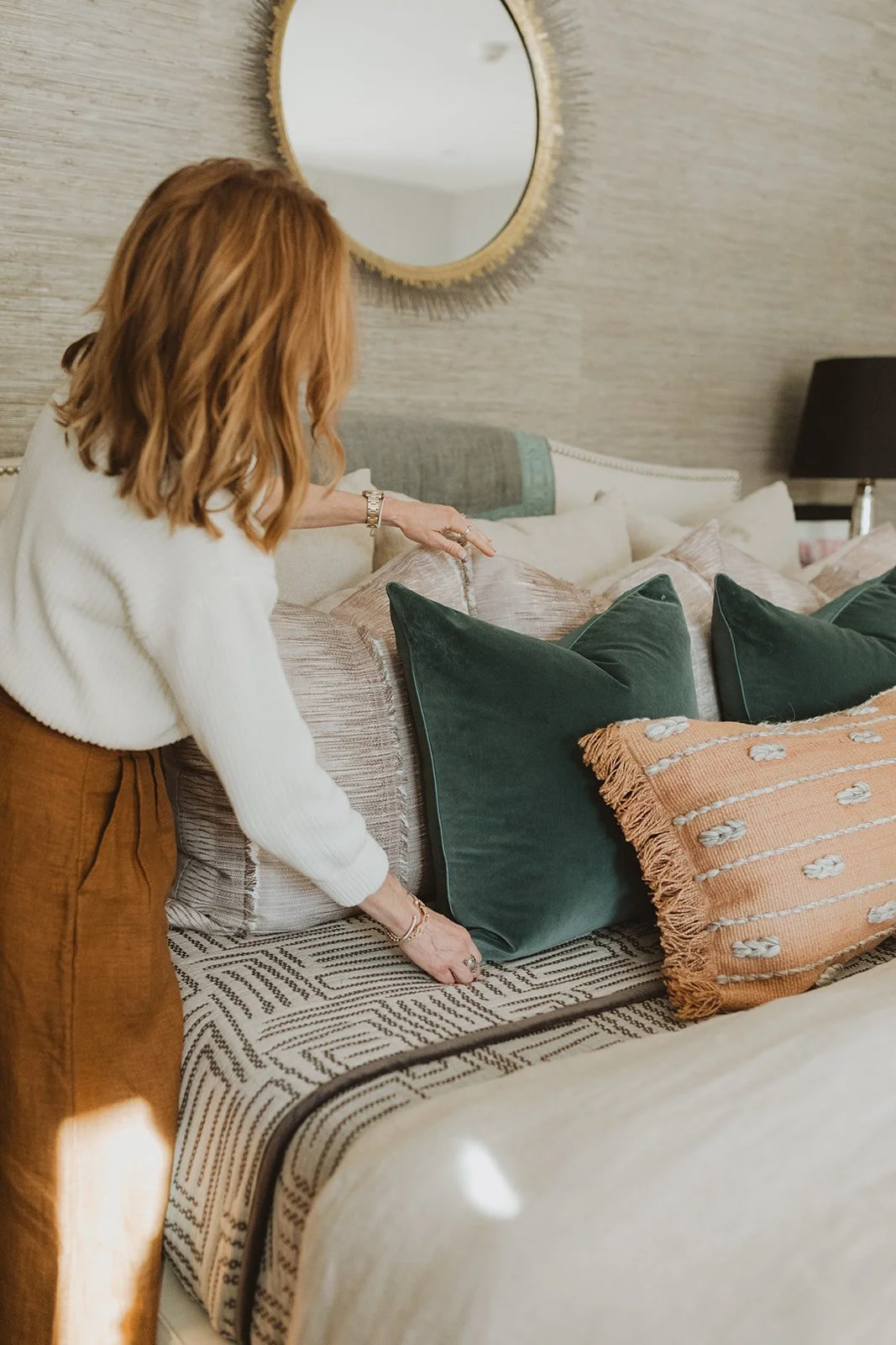 Krista arranging elegant throw pillows on a bed with patterned blankets, enhancing bedroom aesthetics.