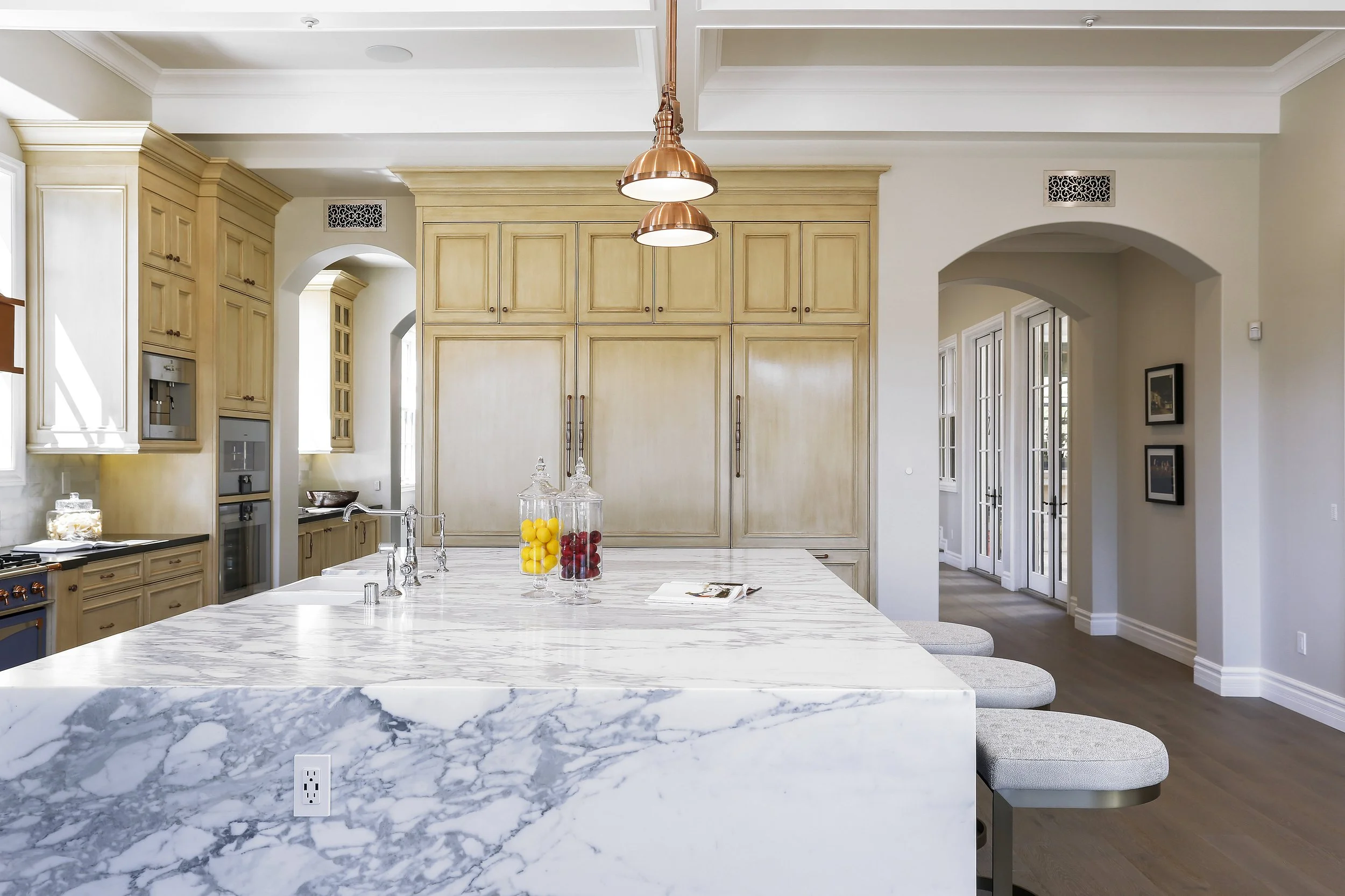 Modern kitchen with marble island, beige cabinetry, and copper pendant lights.