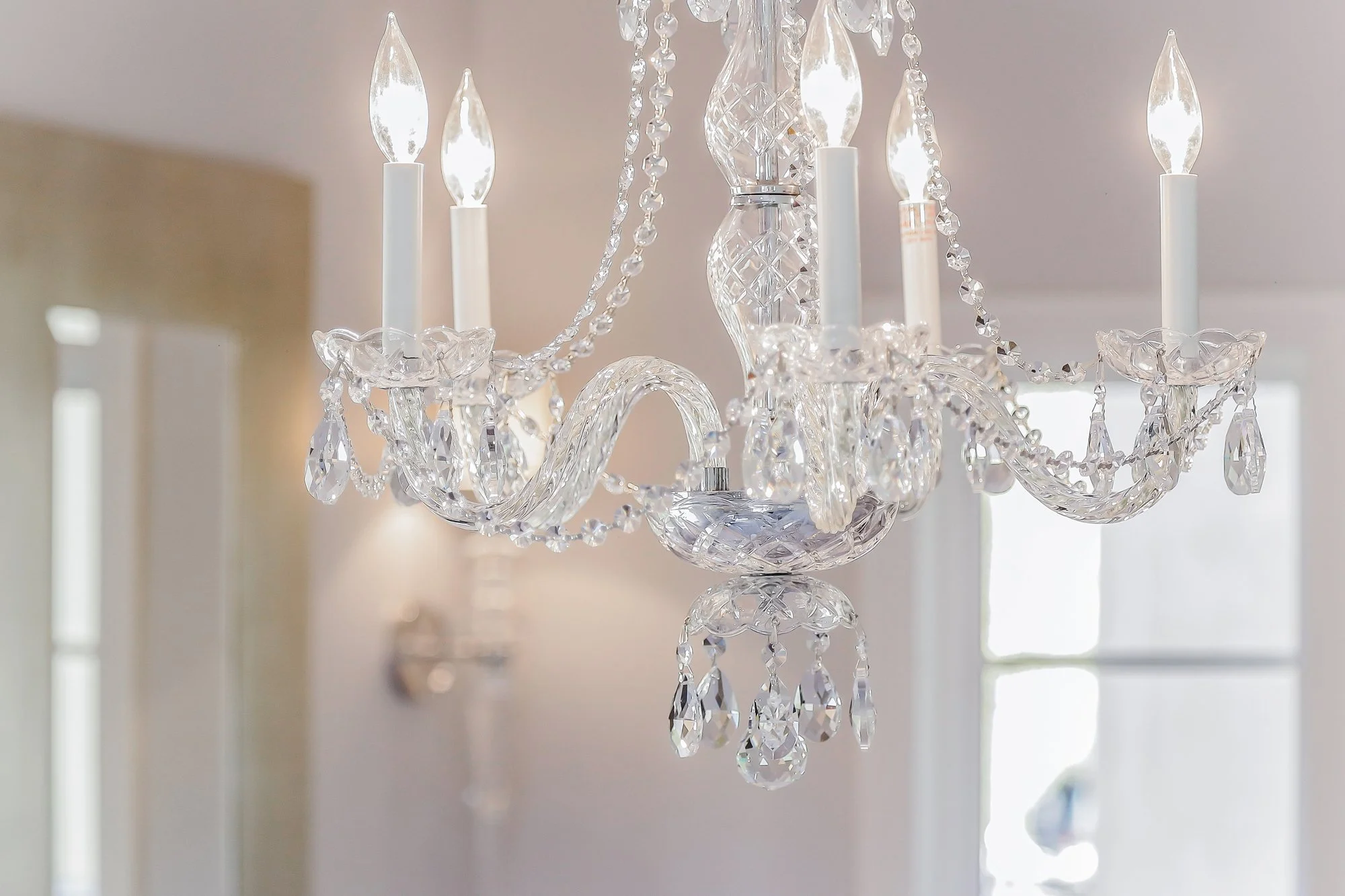A crystal chandelier with candle-shaped light bulbs and hanging crystal beads and prisms.