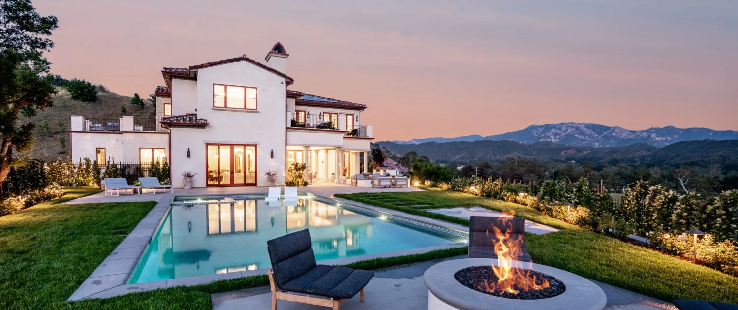 Luxury house with a pool, outdoor fire pit, and mountain view at dusk