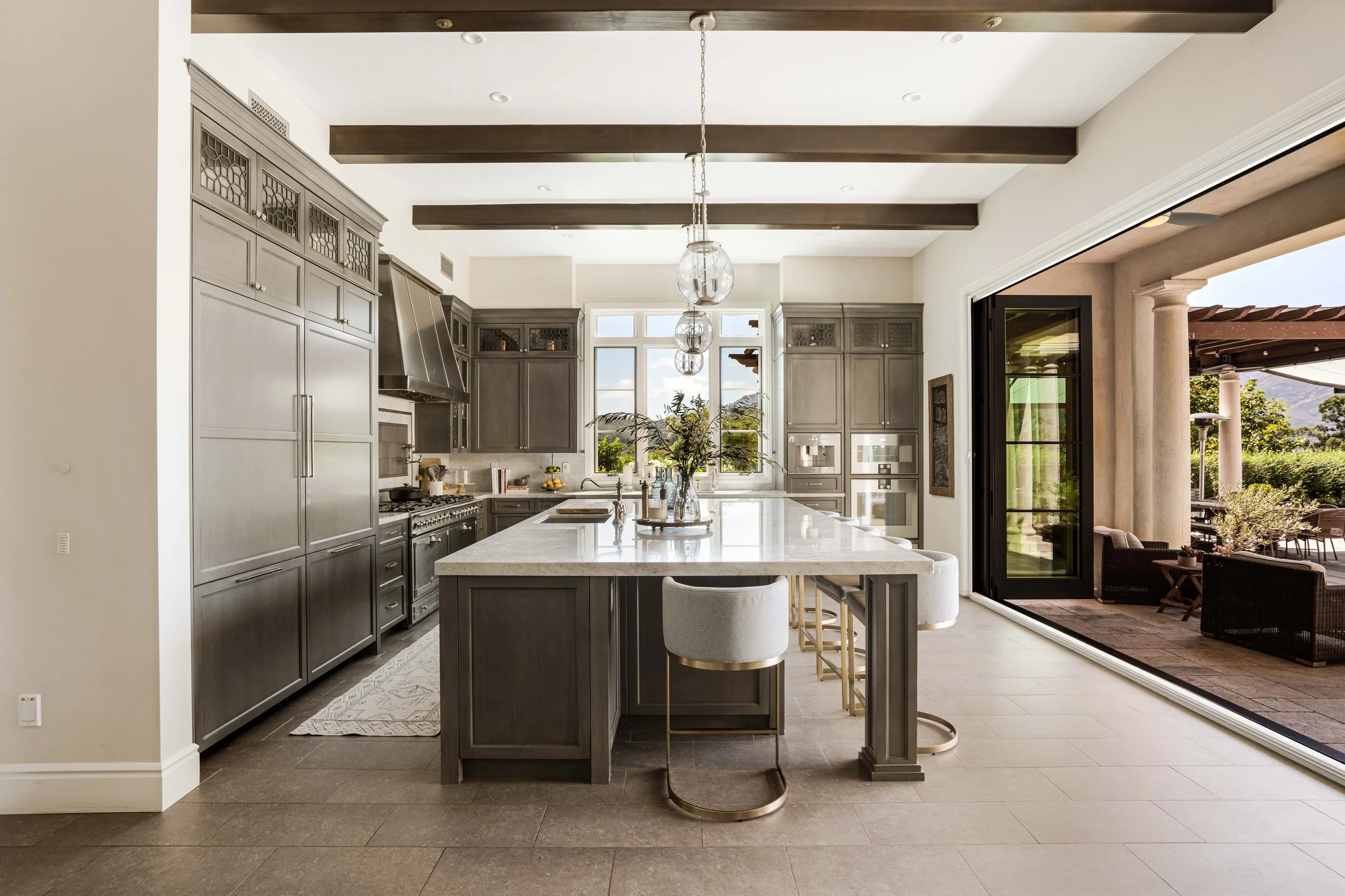Modern kitchen with gray cabinets, white marble island, and large sliding glass door opening to patio with outdoor furniture.