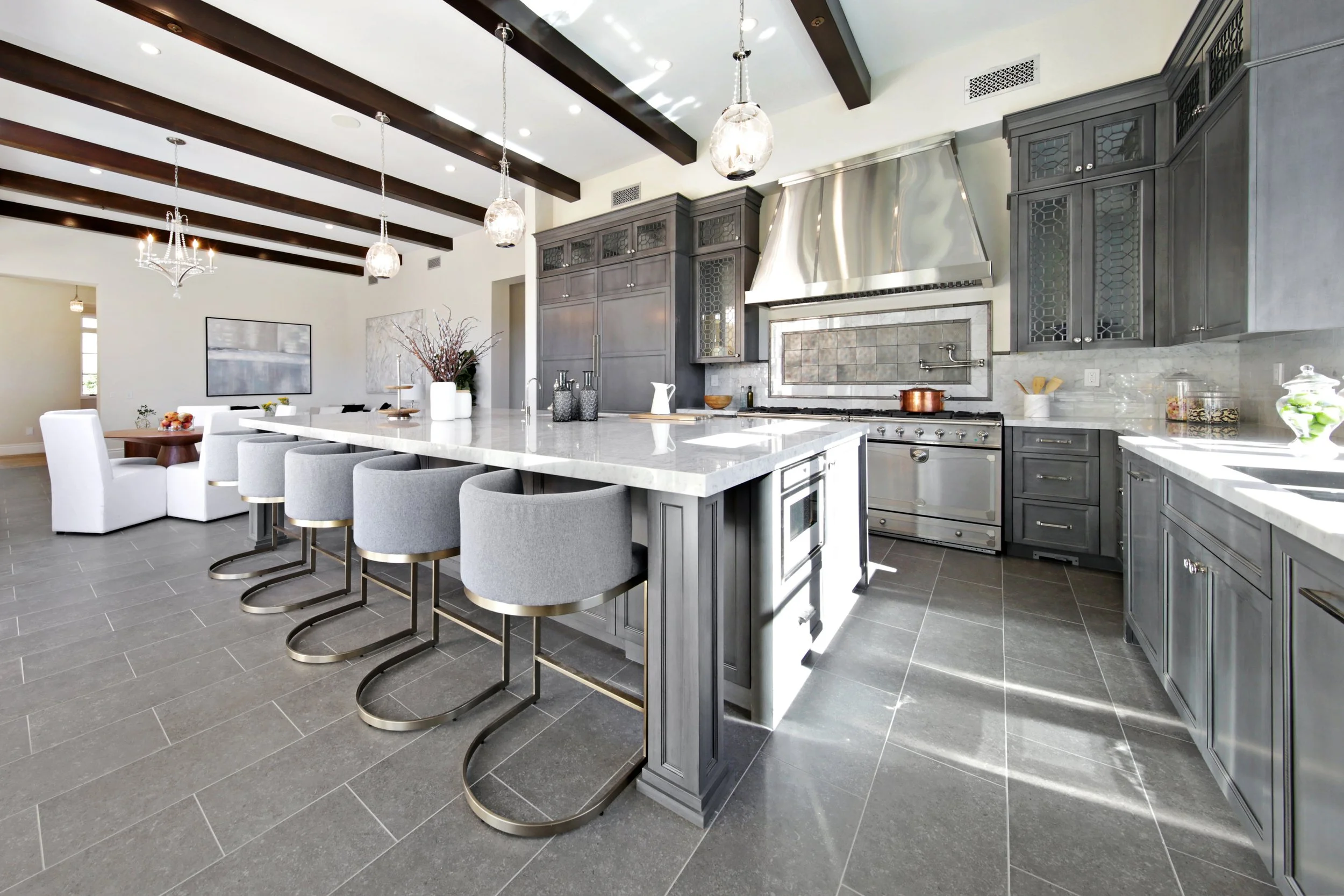 Modern kitchen with gray cabinets, stainless steel appliances, white marble island, gray chairs at the island, and chandelier with glass pendant lights