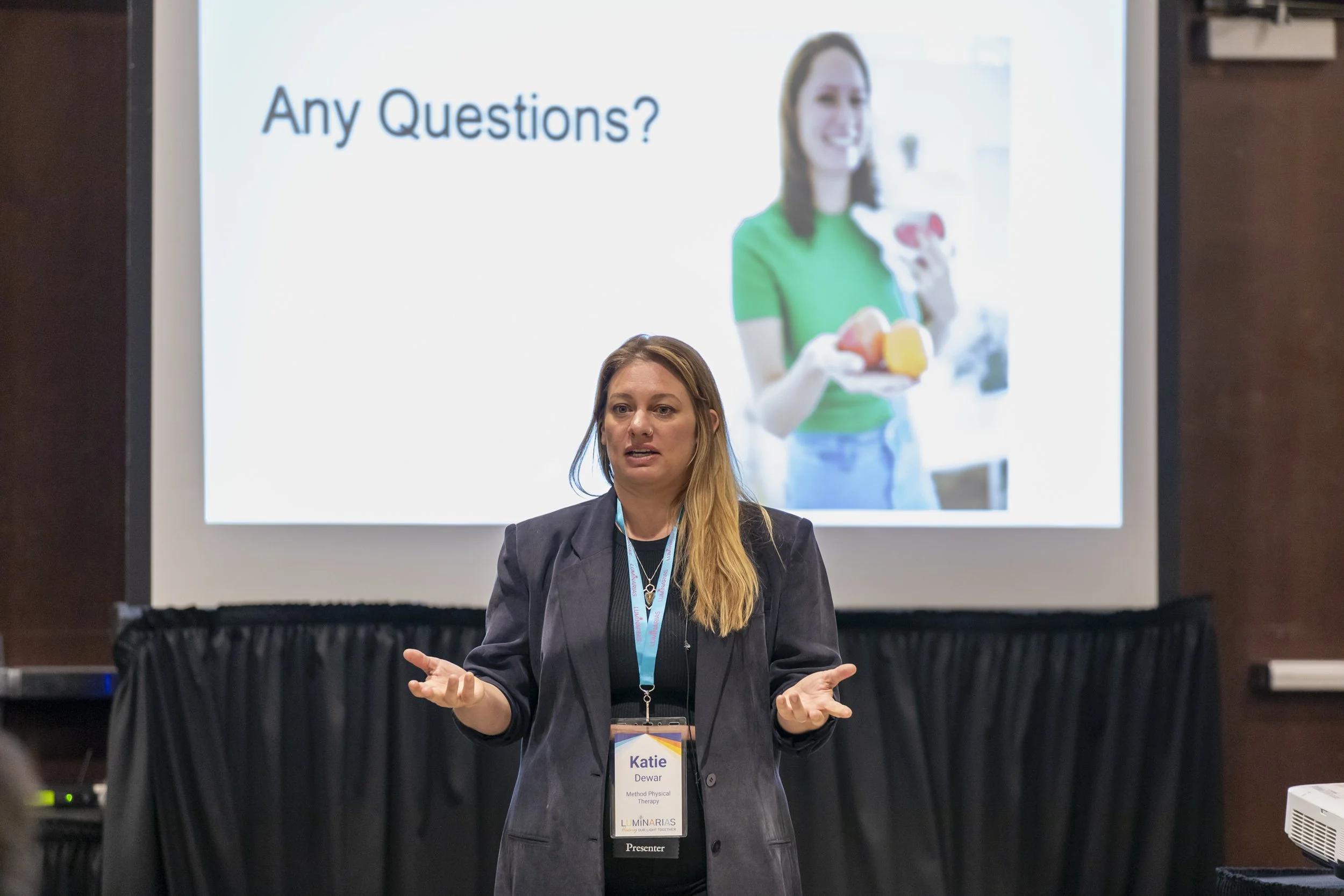 A woman standing before a slide reading "Any Questions?"