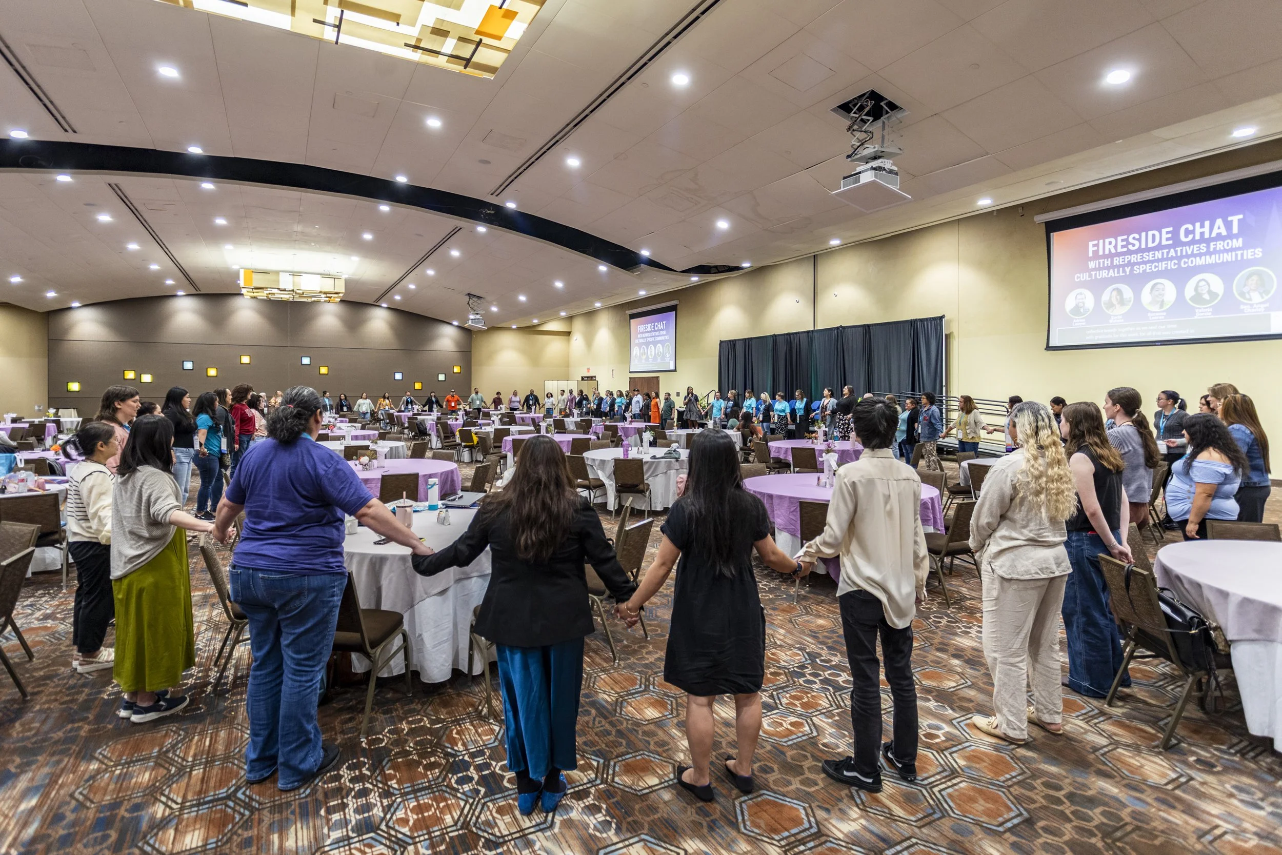 A large group of people holding hands in a circle in a conference room