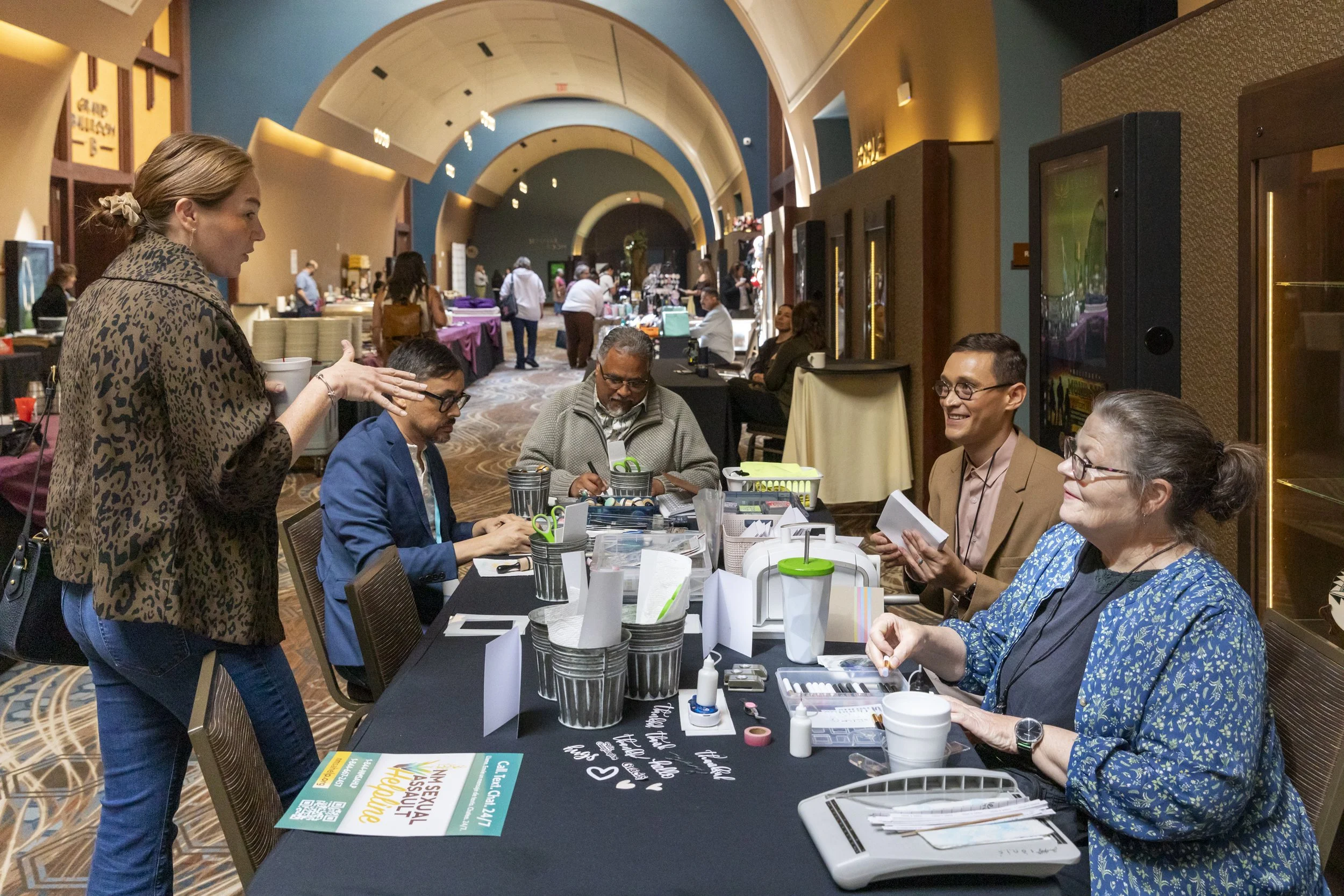 Four people at a table making cards and a fifth standing and talking to them