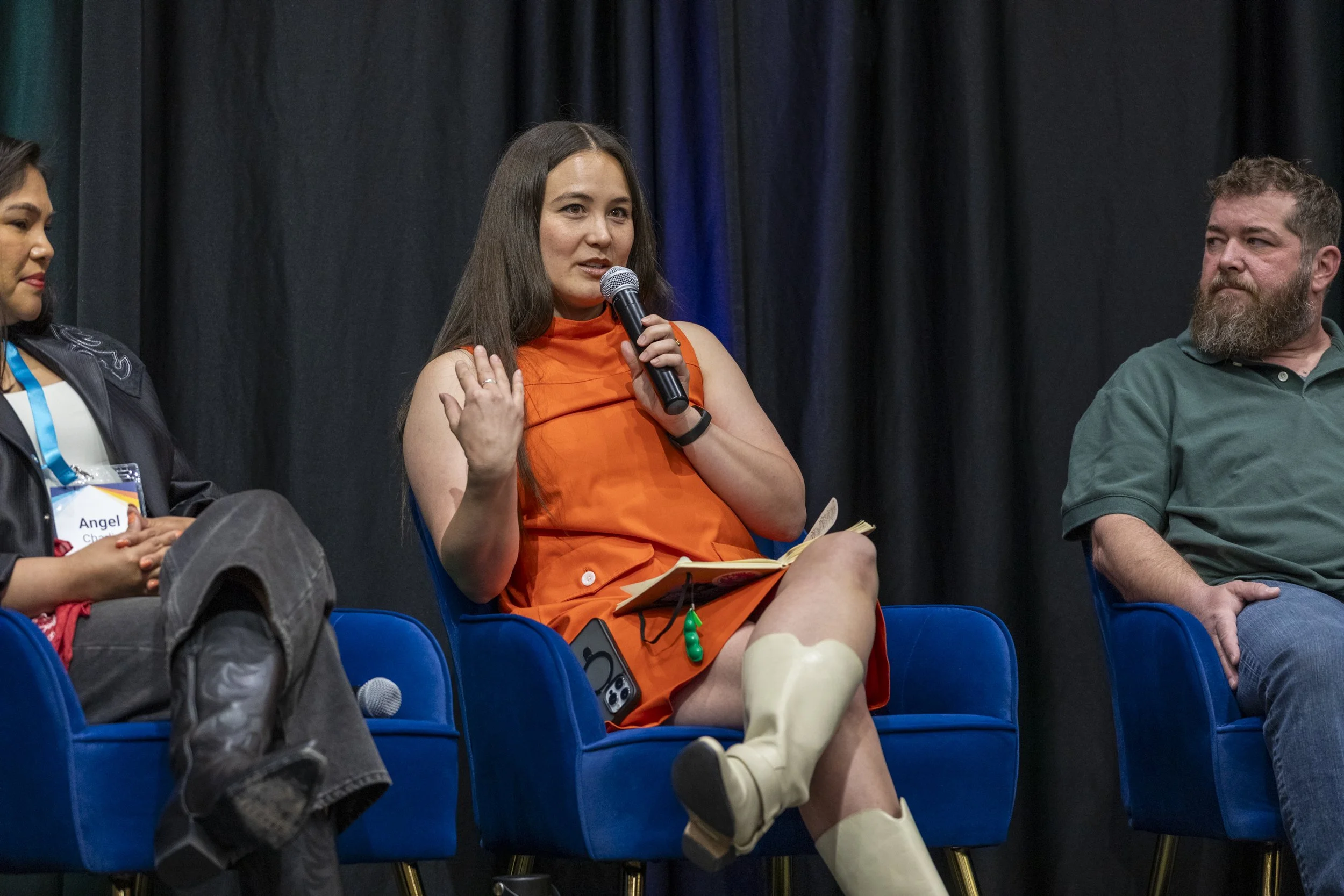 A woman speaking into a mic on stage with two other people