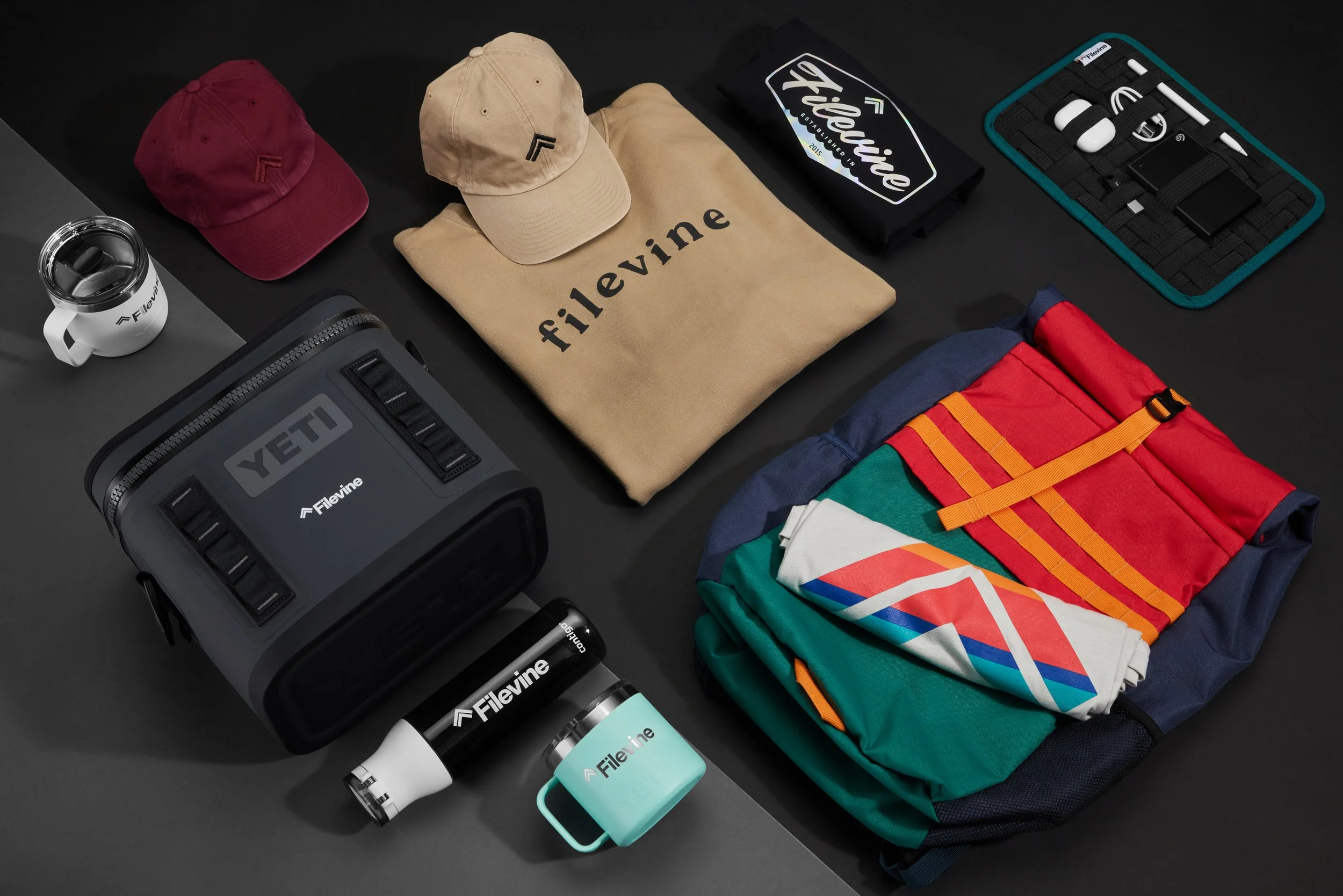Assorted branded merchandise including caps, a sweatshirt, a cooler, water bottles, a mug, a backpack, and an organizer with electronic accessories, featuring 'Filevine' and 'YETI' logos.