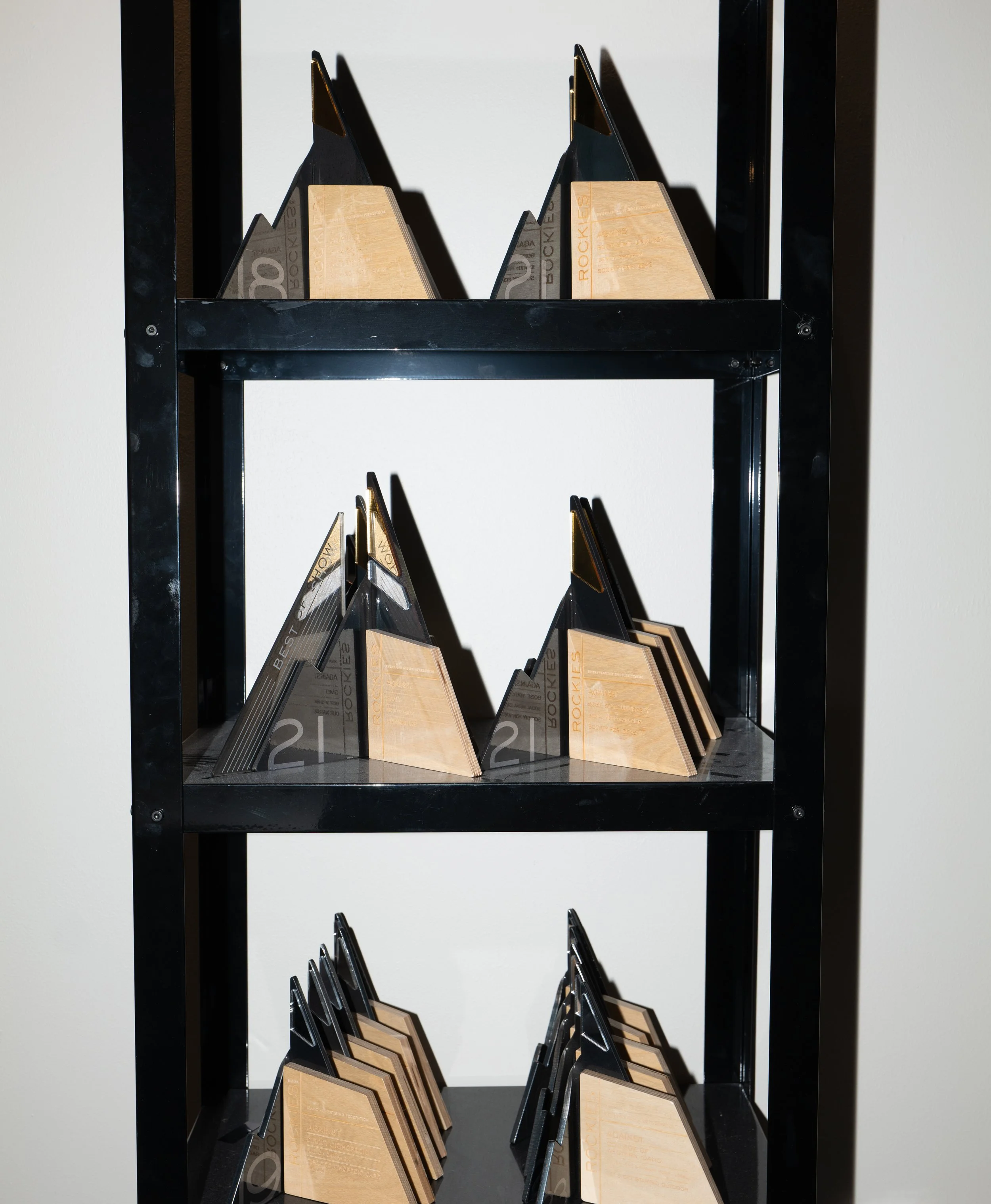 Black shelving unit displaying multiple stacked creative industry awards with geometric black and wood design, showcased against a white wall at the Against office.