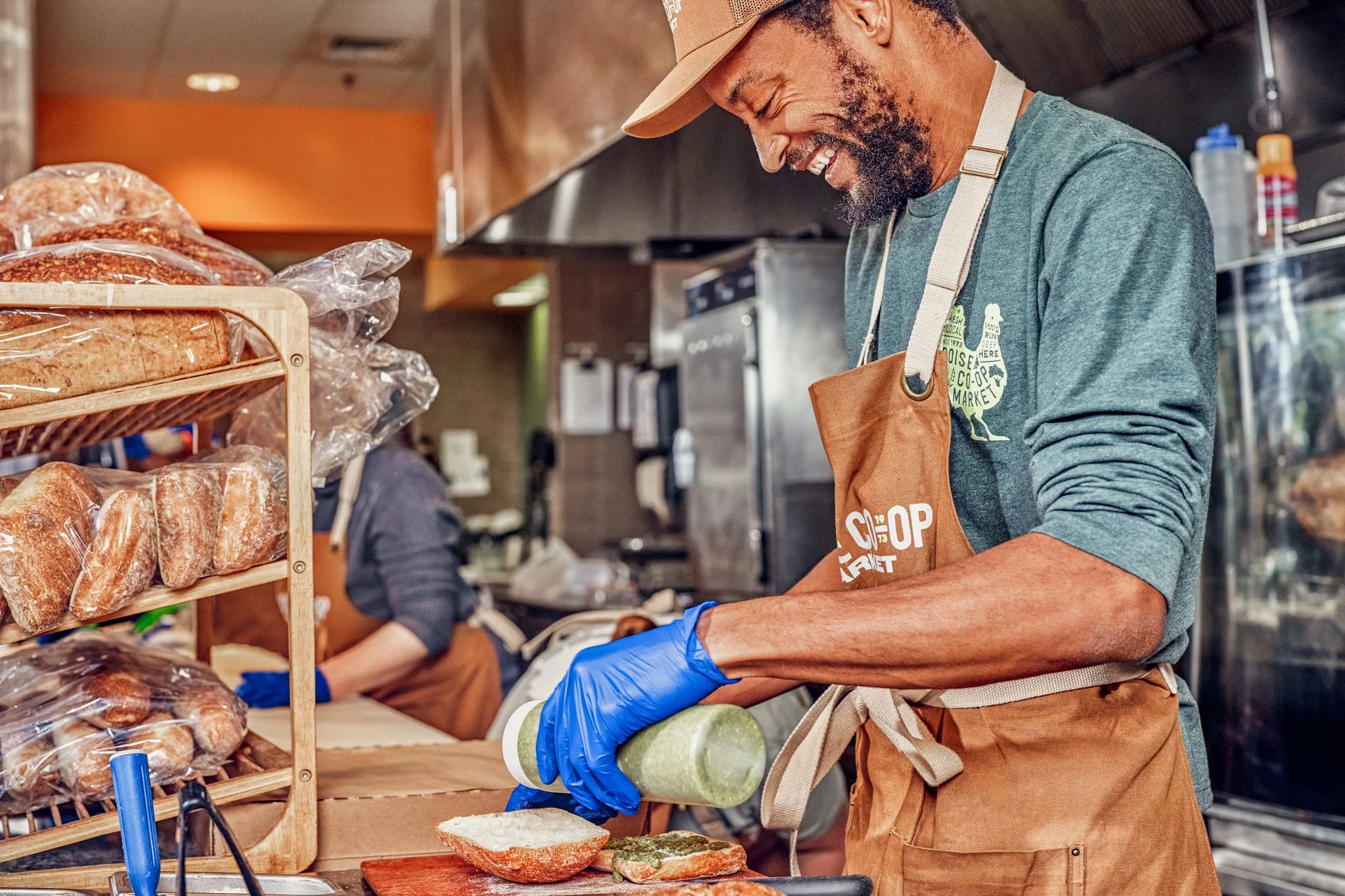 Boise Co-op team member preparing a sandwich and pouring green sauce in the kitchen.