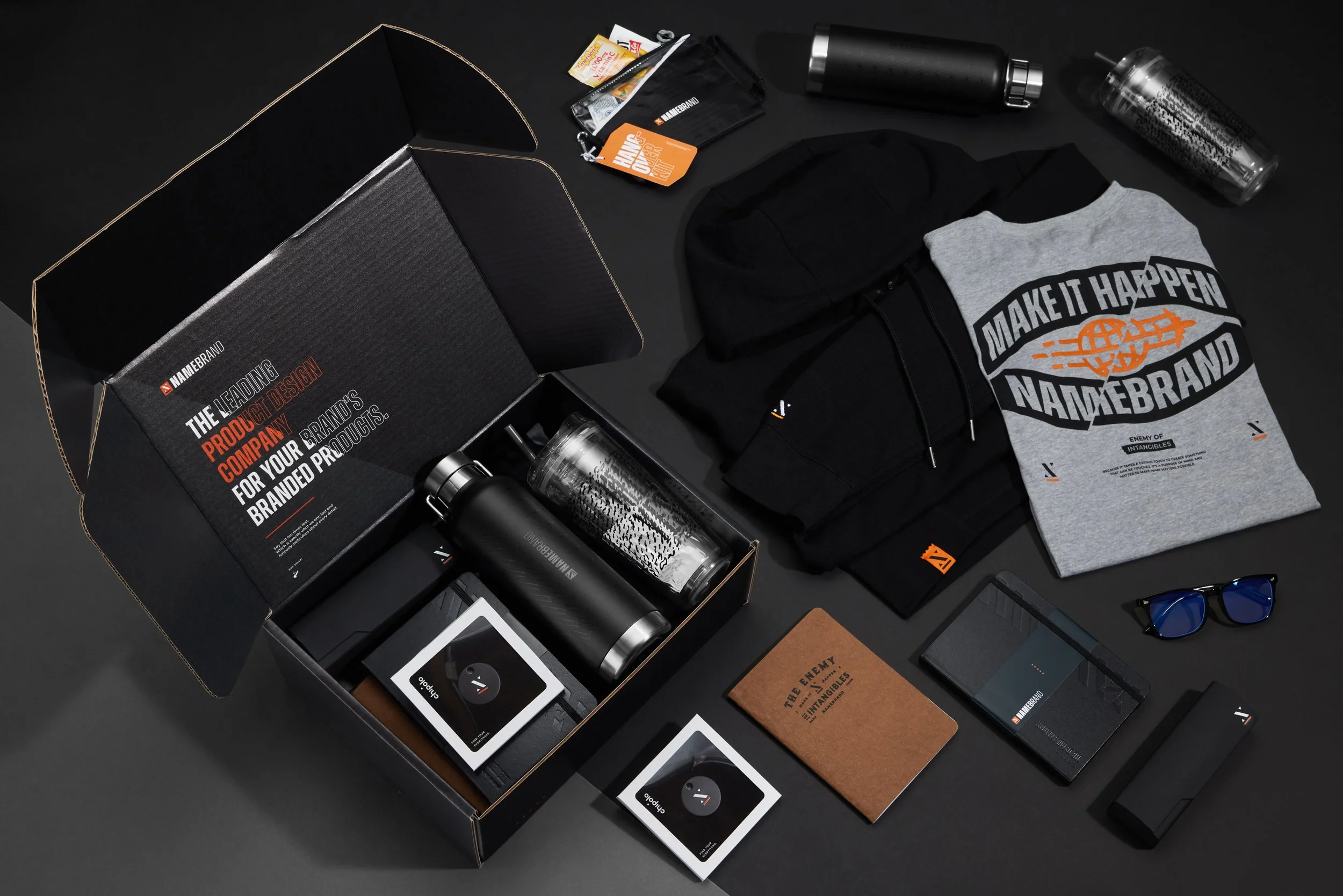 Collection of branded promotional items including apparel, water bottles, notebooks, sunglasses, and a box, laid out on a black surface.