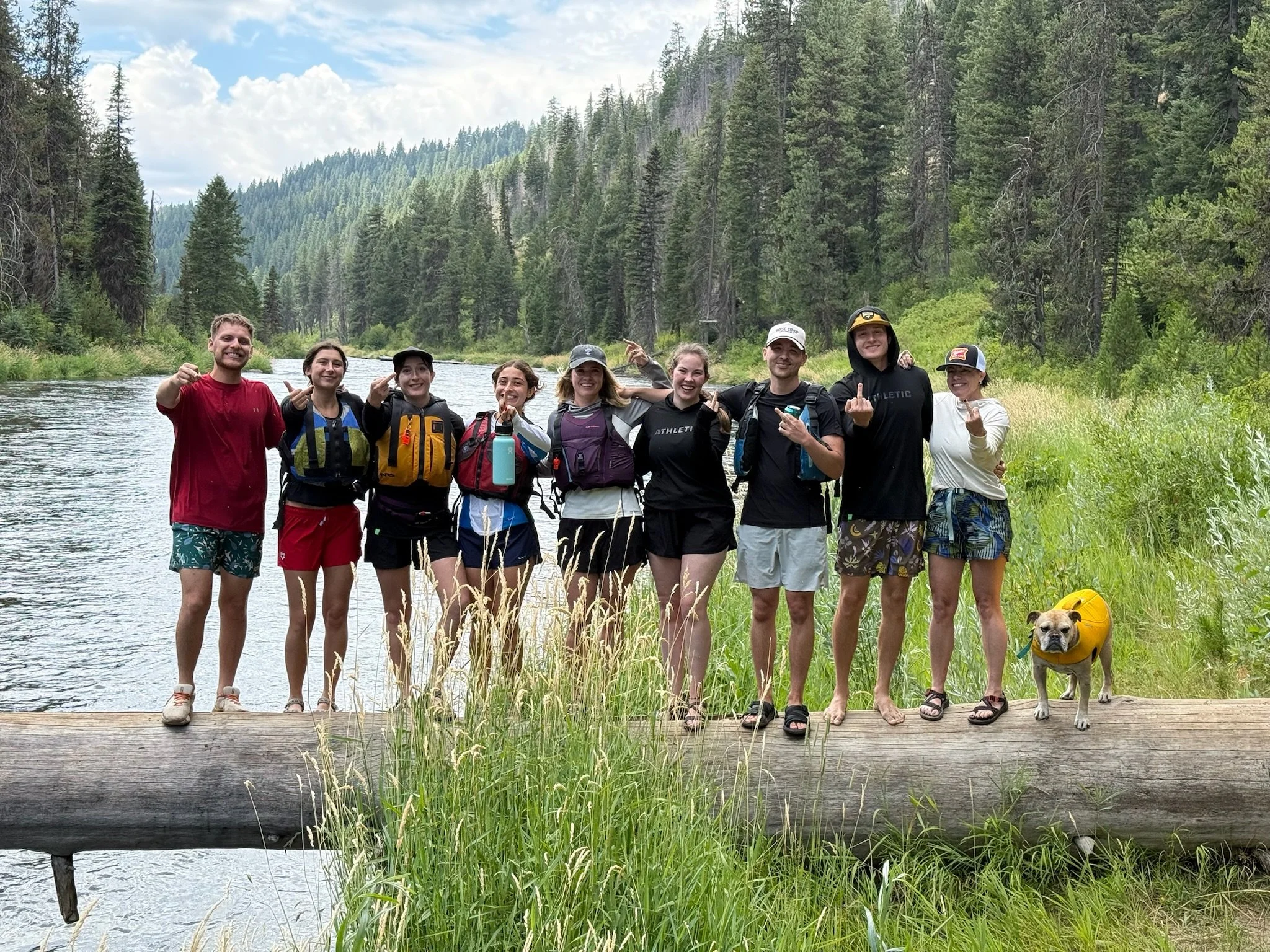 Group of people standing on a log next to a river in the woods
