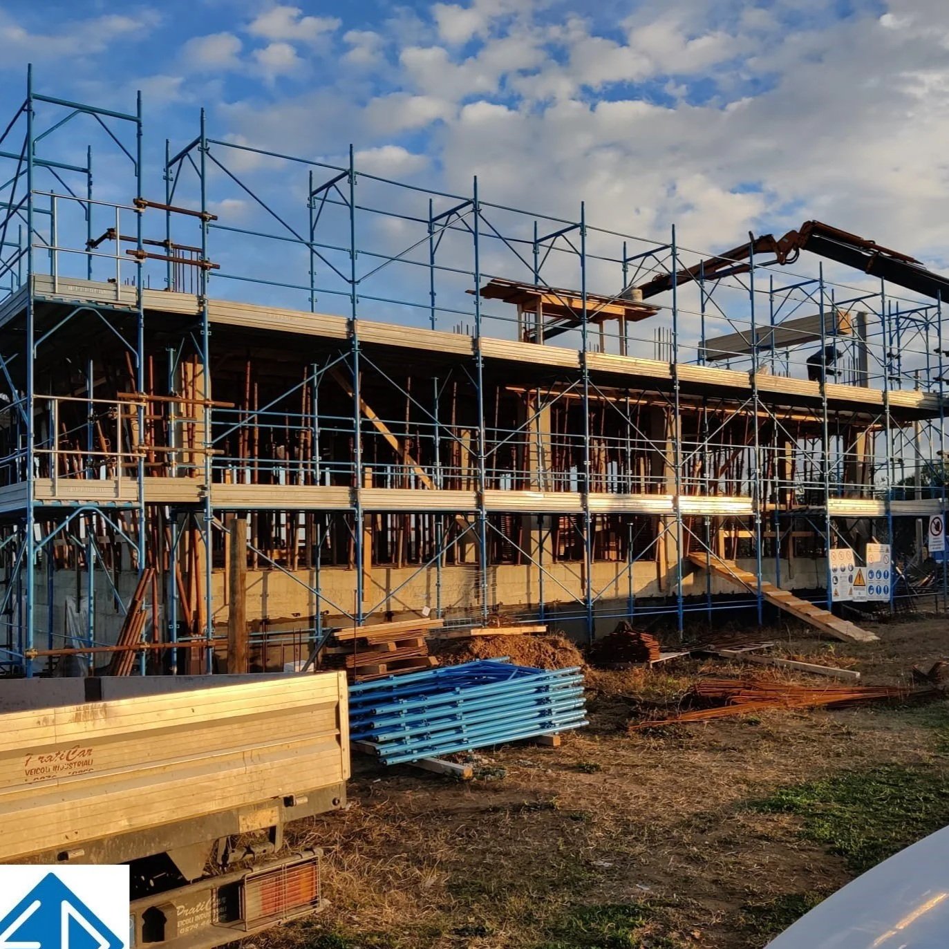 Cantiere edile con struttura in costruzione, impalcature blu e legname, sotto un cielo con nuvole