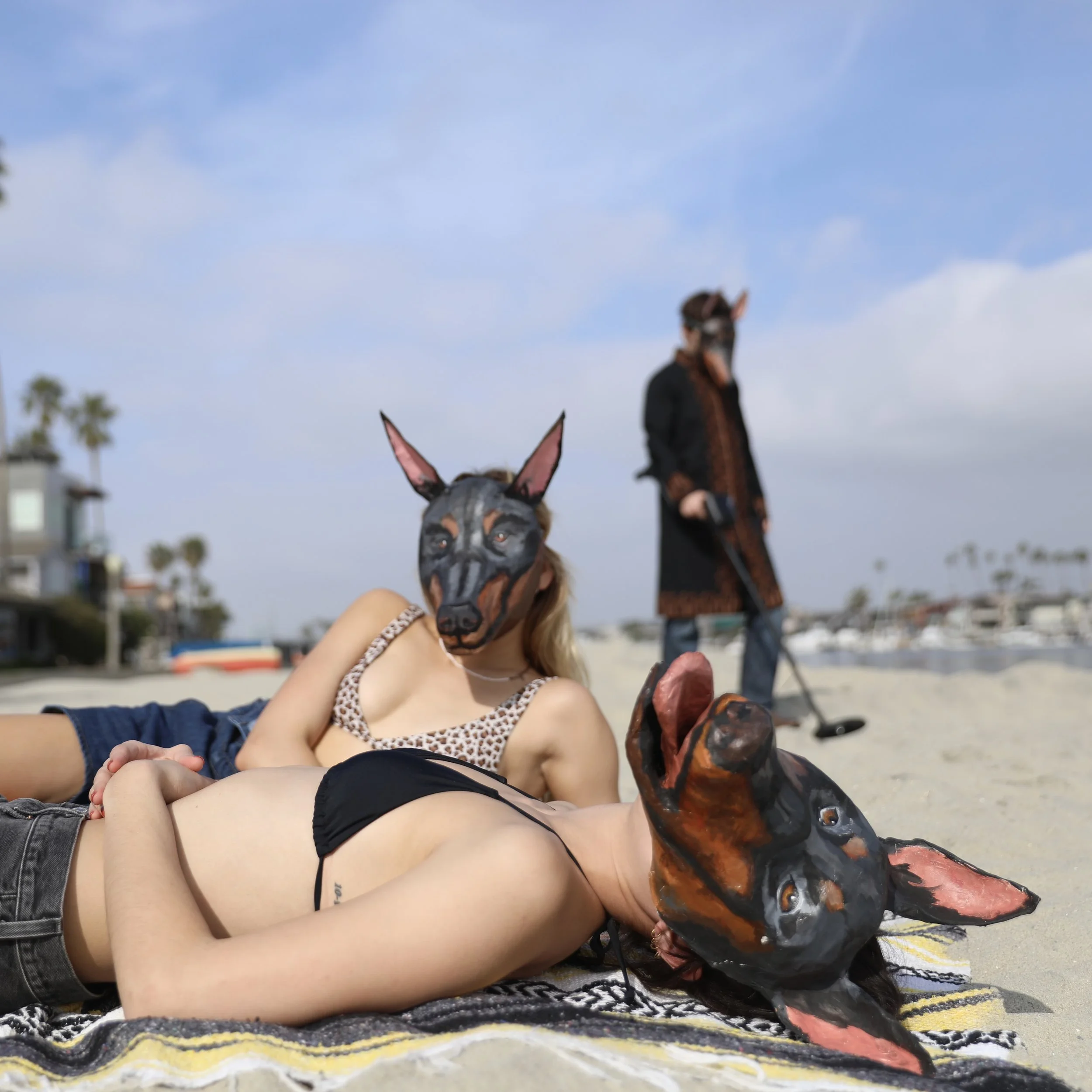 Doberman dogface masks by contemporary artist Giana Amantea, modeled by three people on a beach. Masks by contemporary artist Giana Amantea.