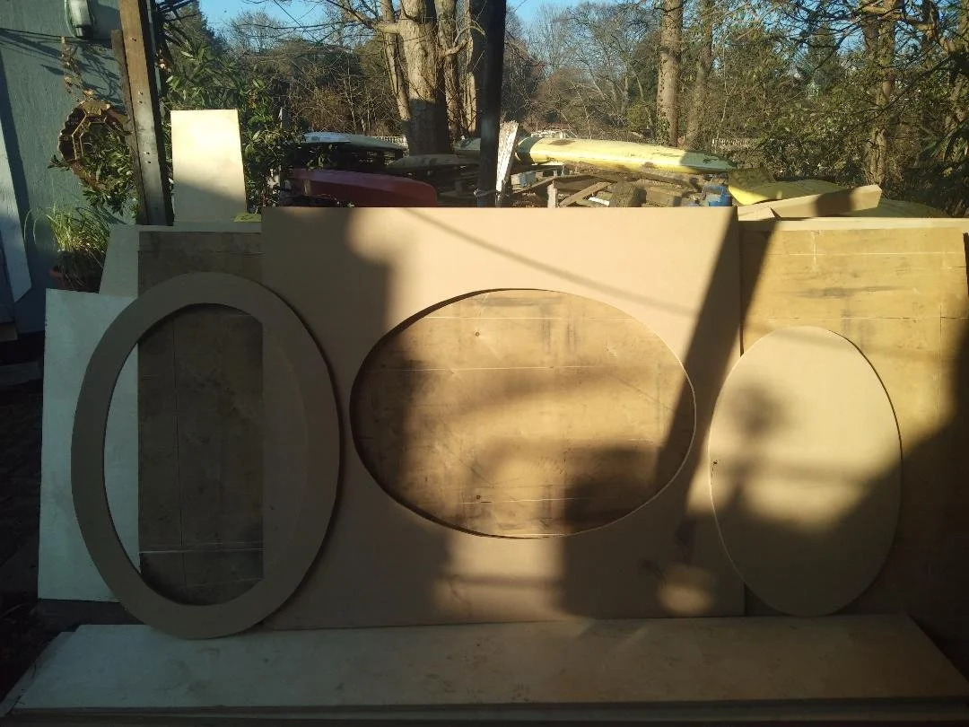 Assorted wooden boards and cutouts with oval shapes leaning against a wall, outdoors.