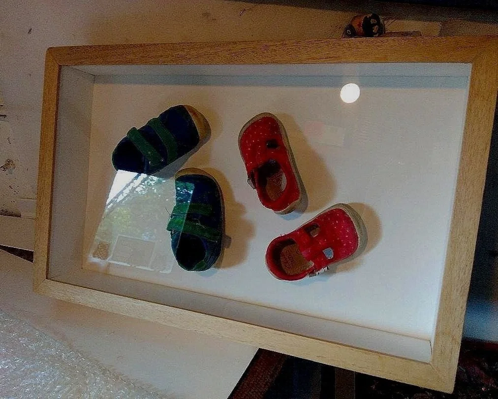 Framed display with four baby shoes, two blue and two red, arranged on a white background. Where to frame artwork professionally in Somerset by Tyler Studios