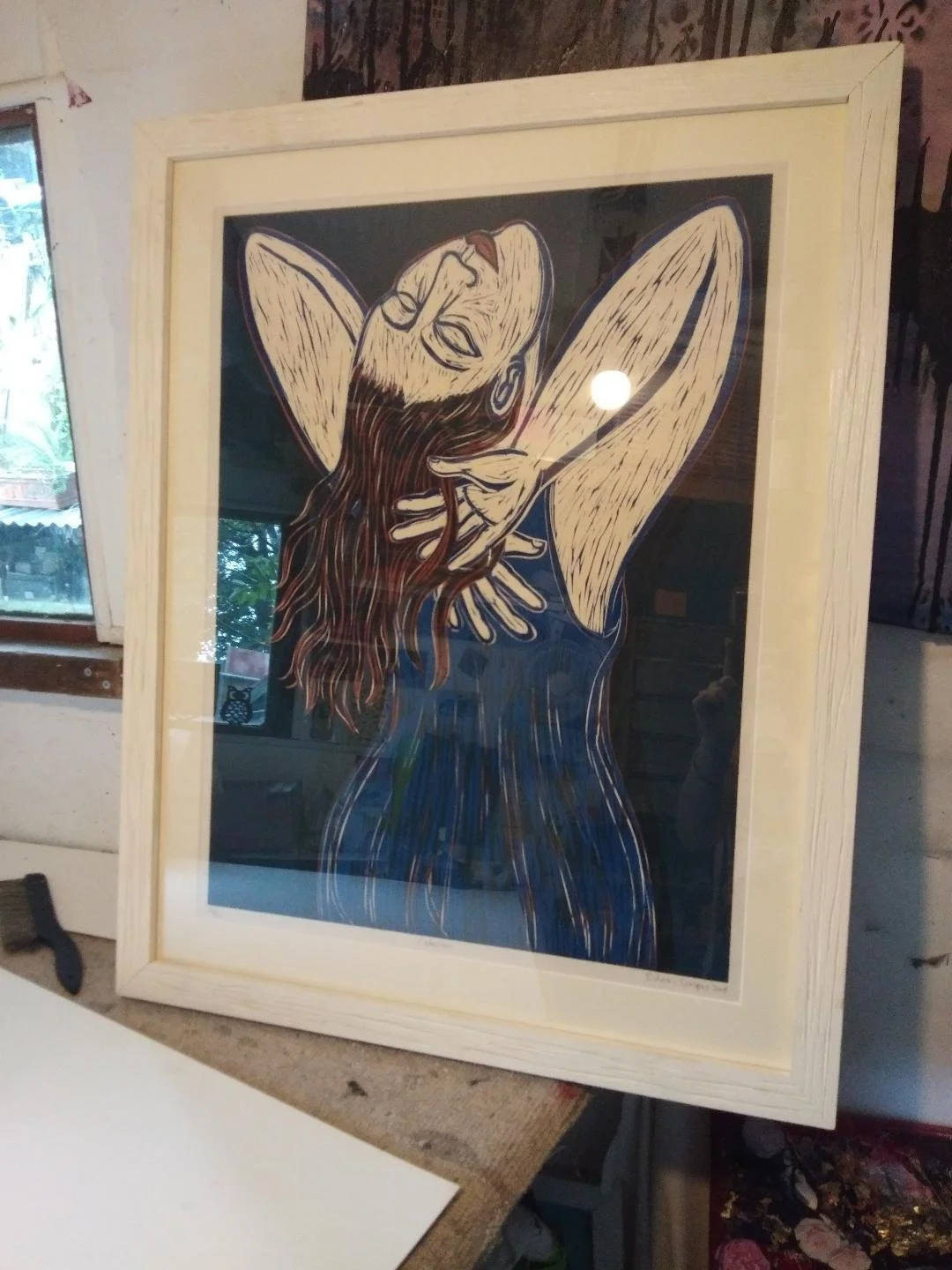 Framed artwork depicting a stylized figure with long hair and arms raised, displayed in a room.  Personalized picture framing service in England