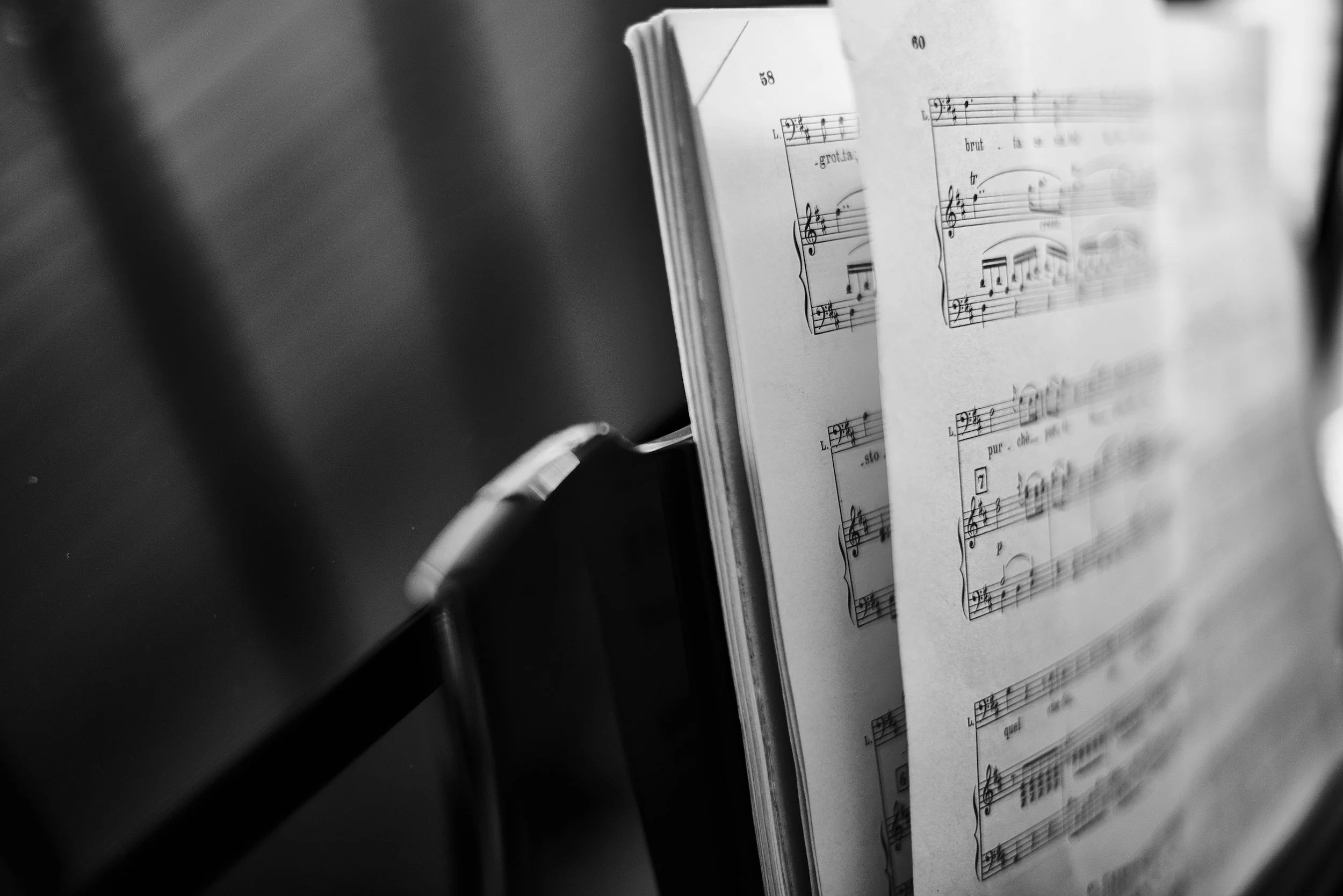 A black and white photograph of a music sheet book open, displaying musical notes and lyrics, viewed at an angle.