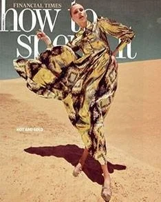 Person in a patterned yellow dress walking through a desert setting under blue sky. Magazine cover text: 'Financial Times, how to spend it'."