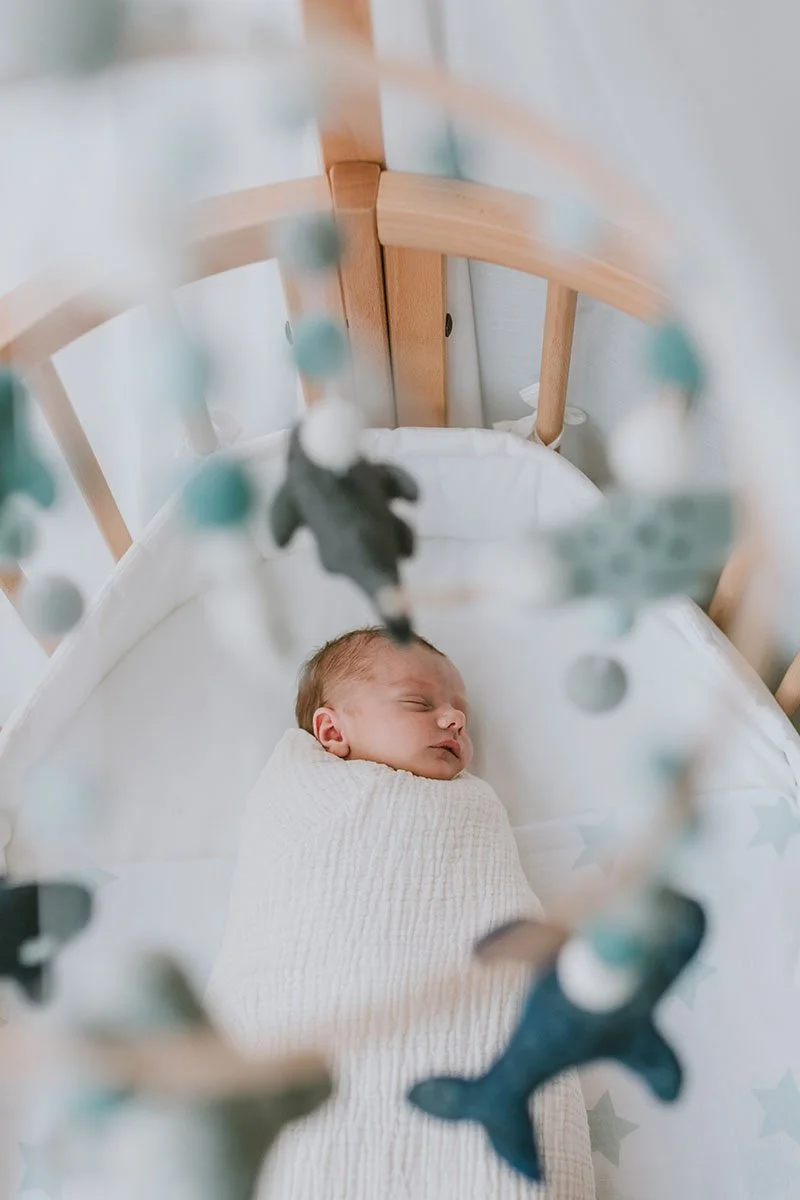 Newborn sleeping in crib below mobile with blue toys