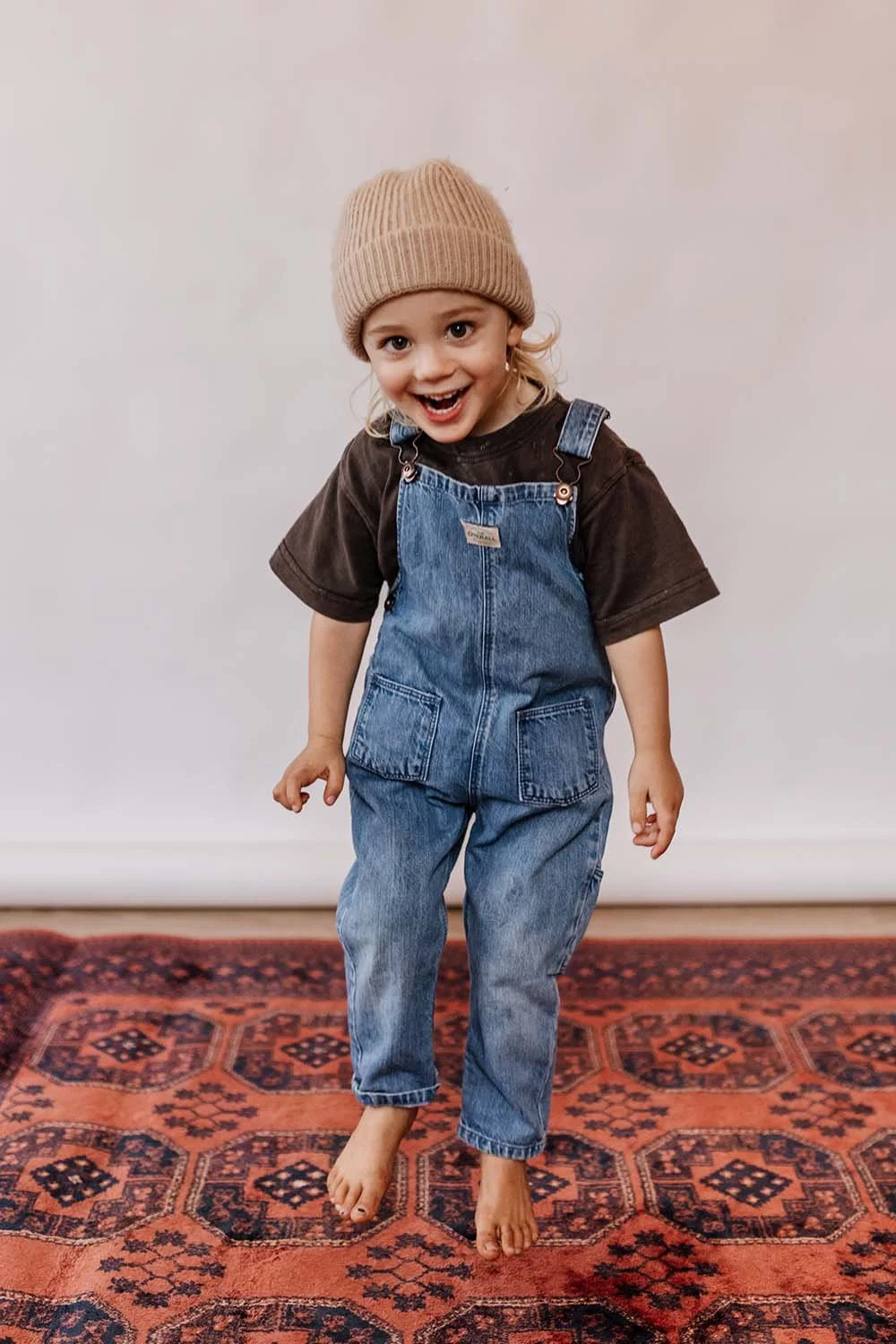 Kids photo of young boy in denim overalls and beanie having fun