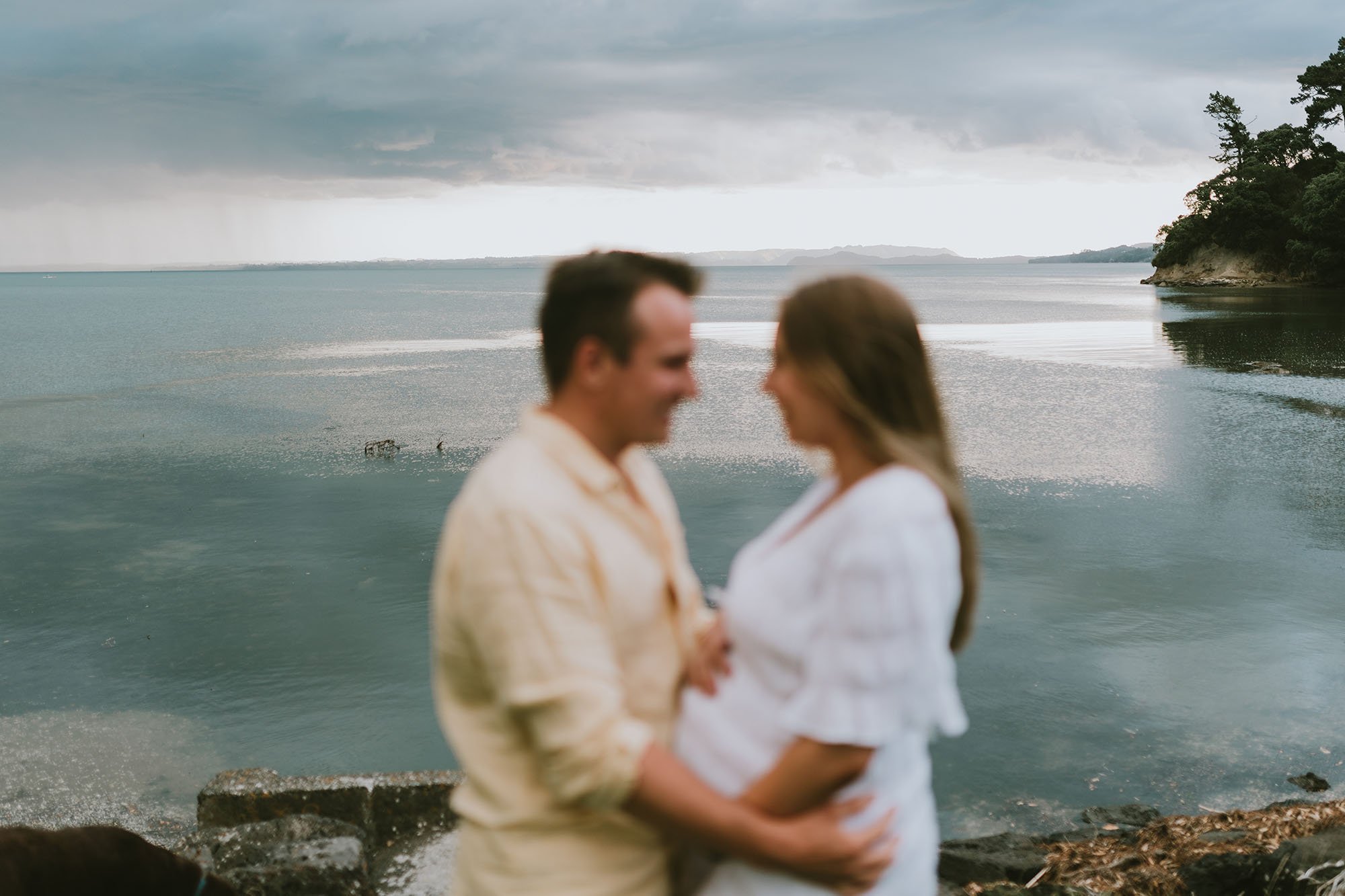 Maternity shoot couple holding bump overlooking bay in NZ