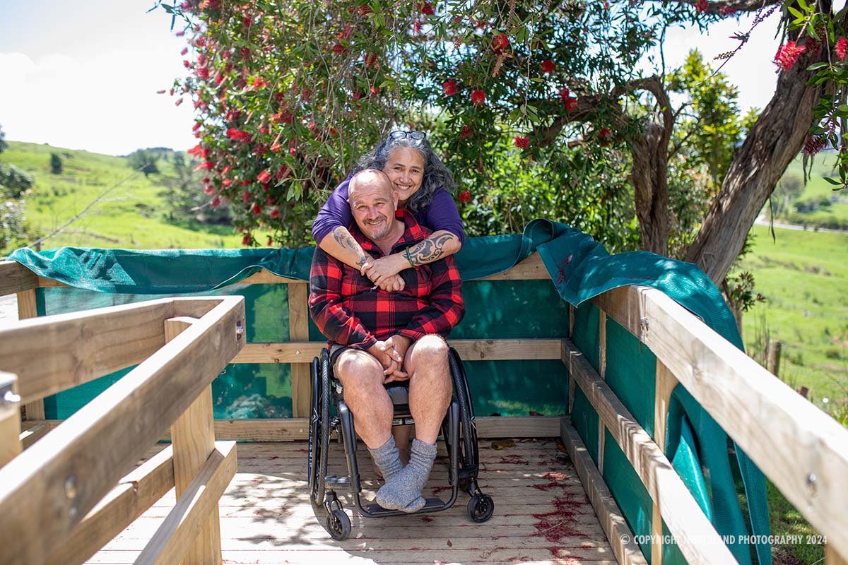 Wife and husband in wheelchair at their home hugging and smiling.