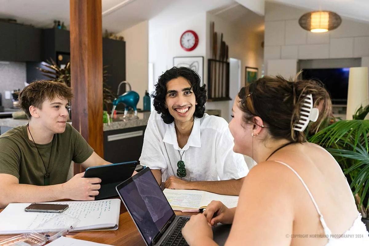 Students working at table at home, boy with pounamu smiling at camera for stock photo