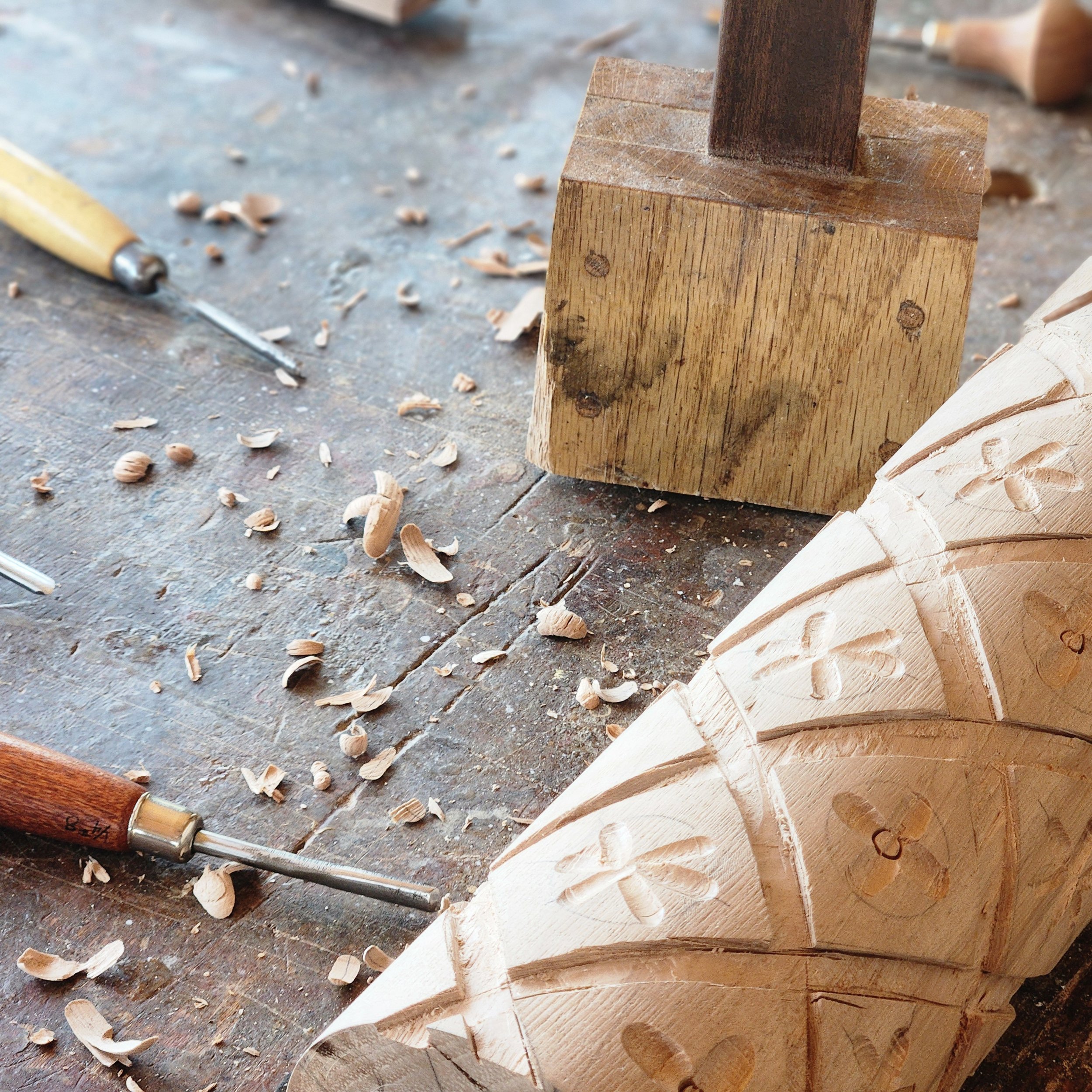 Close-up of a woodworking workspace with a wooden block, wood shavings, and a carving tool on a workbench.