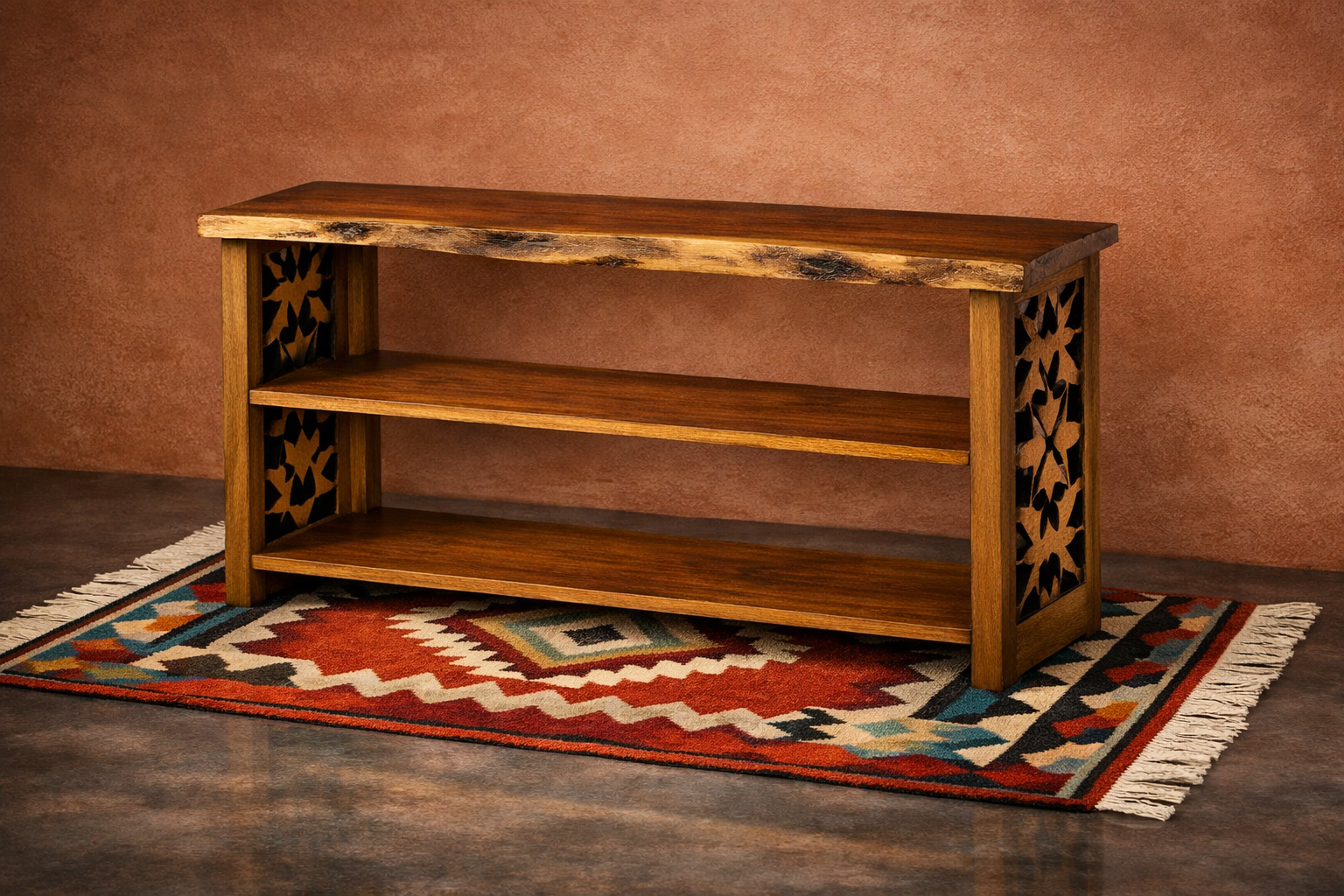 A wooden bookshelf with three shelves, decorated with carved floral patterns on the sides, sits on a colorful patterned rug against a textured reddish-brown wall.