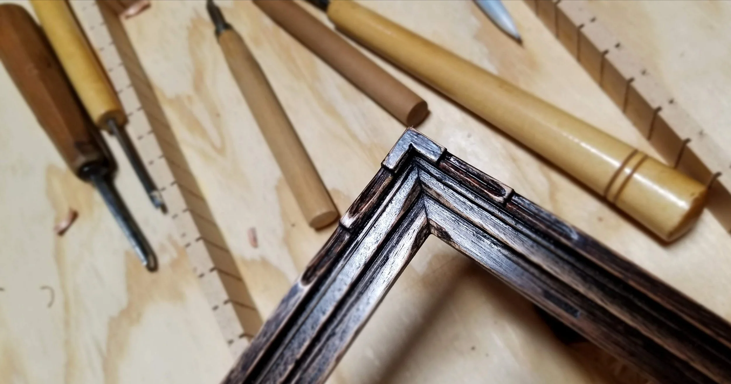 Handmade picture frame on a workbench with woodworking tools and wooden rods nearby.