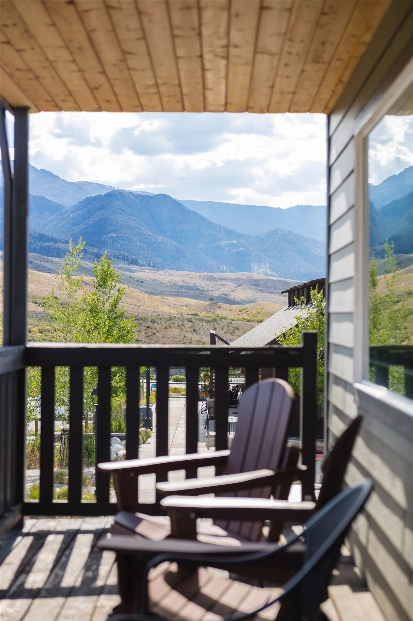 View from a porch showing mountains, cloudy sky, and a backyard with chairs and trees.