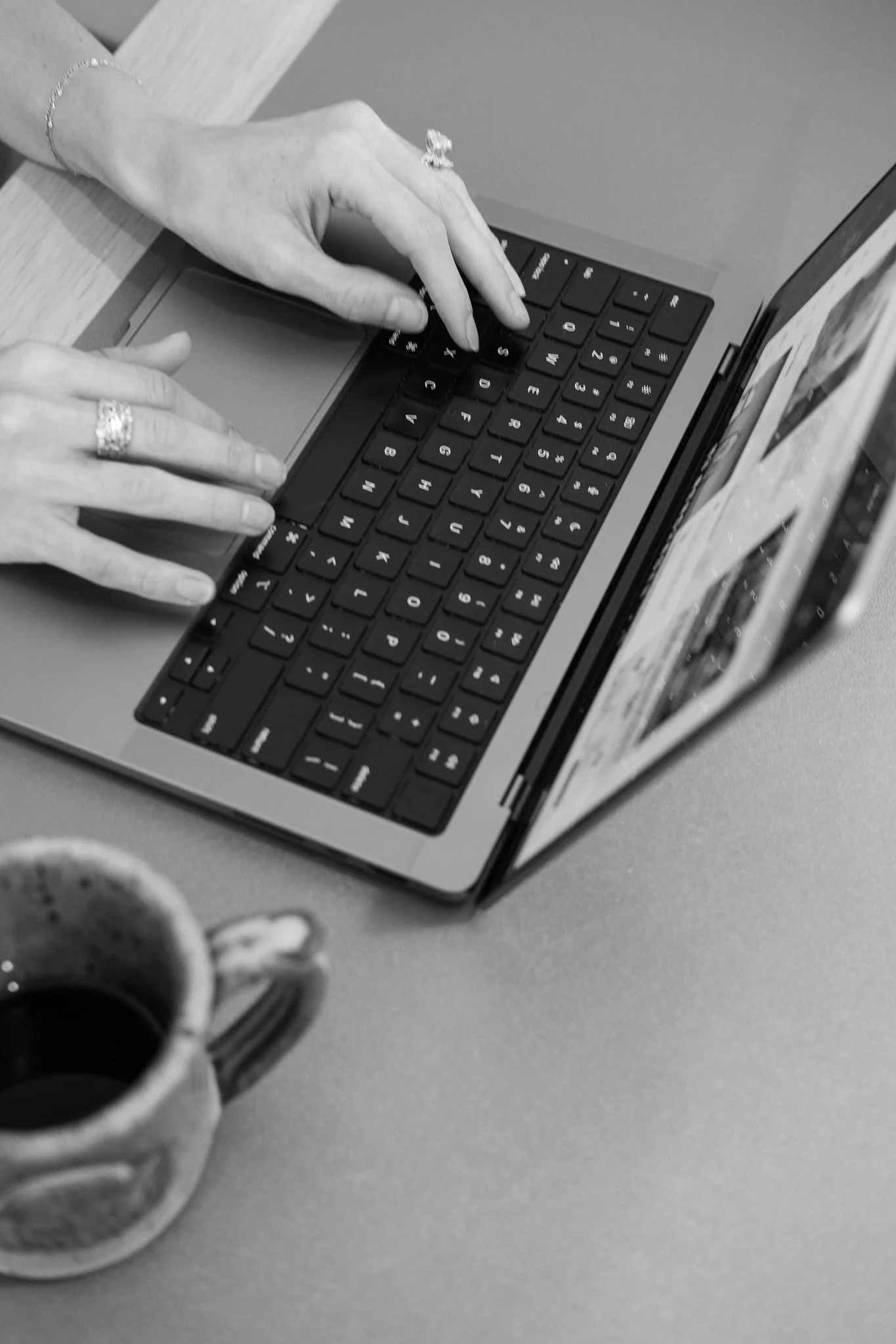 A person typing on a laptop keyboard with a coffee mug nearby.
