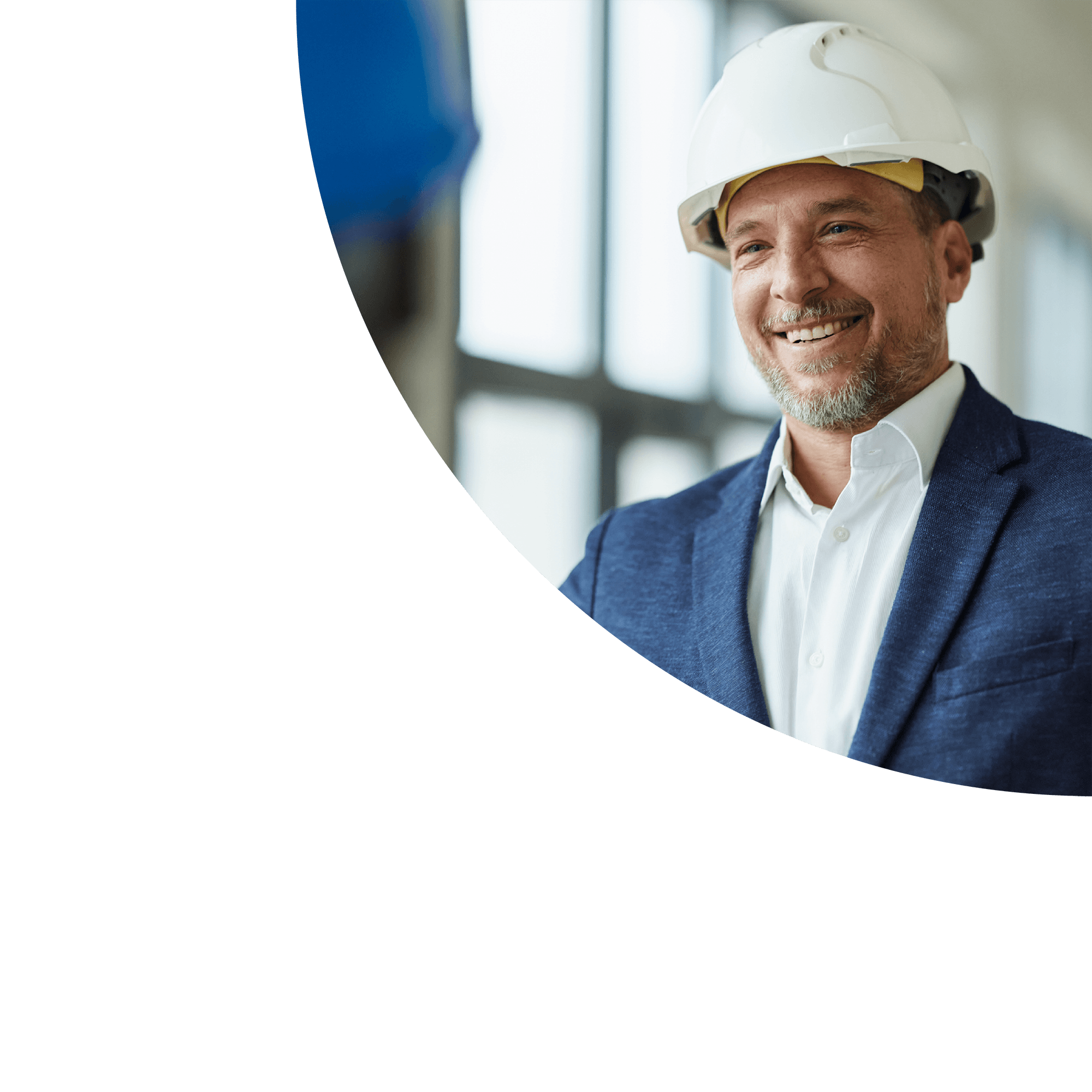 Smiling man wearing a white hard hat, white shirt, and blue blazer, indoors near a window.