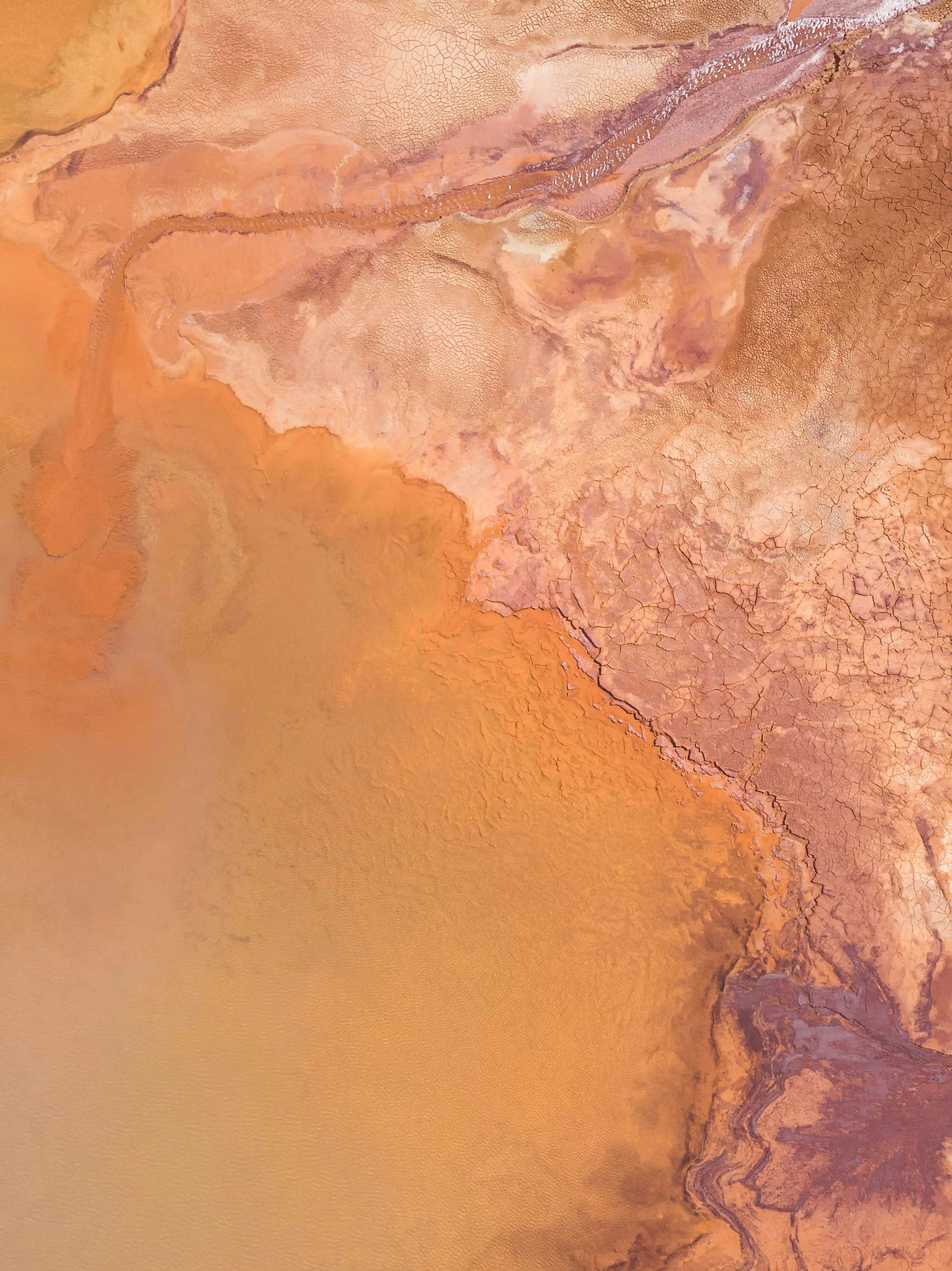 Close-up of a landscape with reddish-brown cracked earth and dry, winding river or canyon. The terrain appears arid and desert-like.
