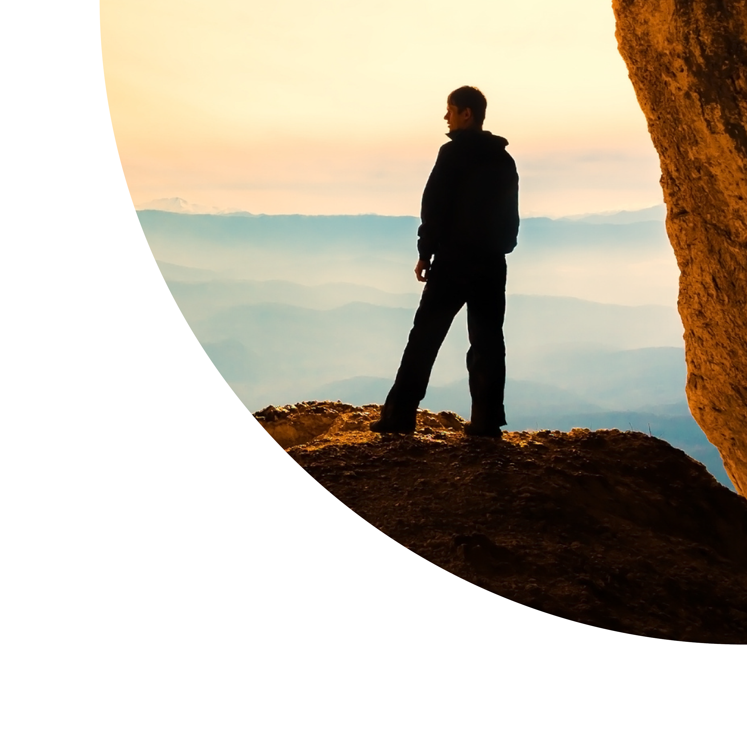 Silhouette of a man standing on a rocky ledge with mountains and a colorful sunset in the background.