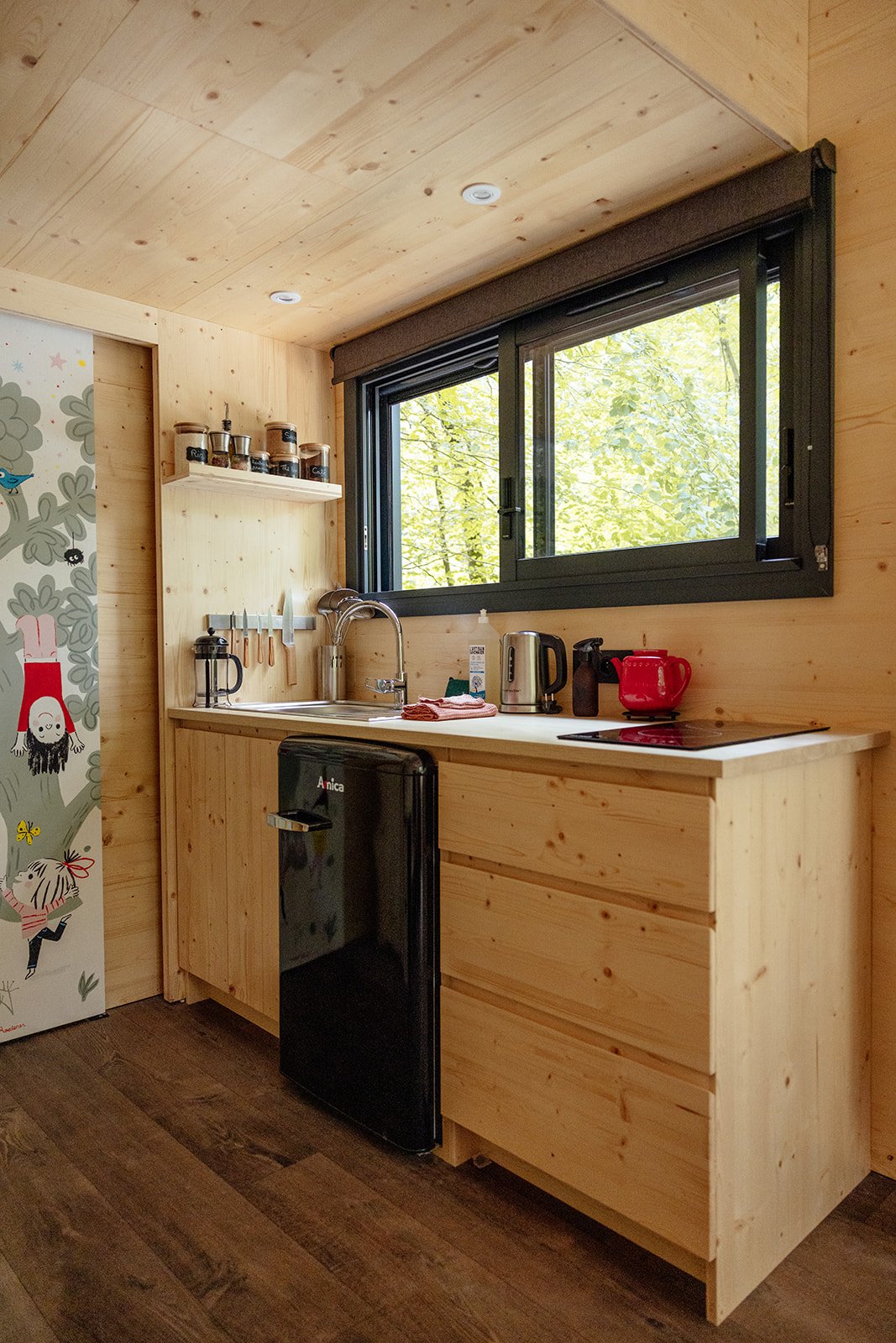 Petite cuisine en bois avec un évier, des appareils électroménagers, une fenêtre donnant sur la nature.