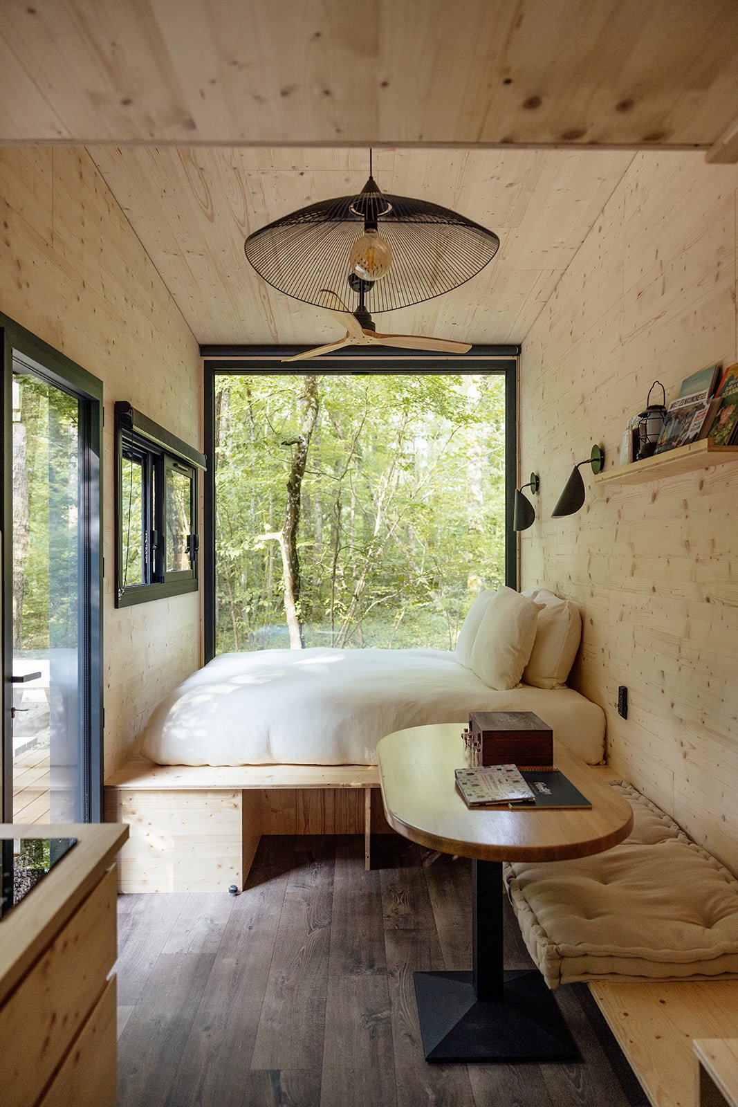 Chambre en bois avec un lit à côté d'une grande fenêtre offrant une vue sur la forêt.