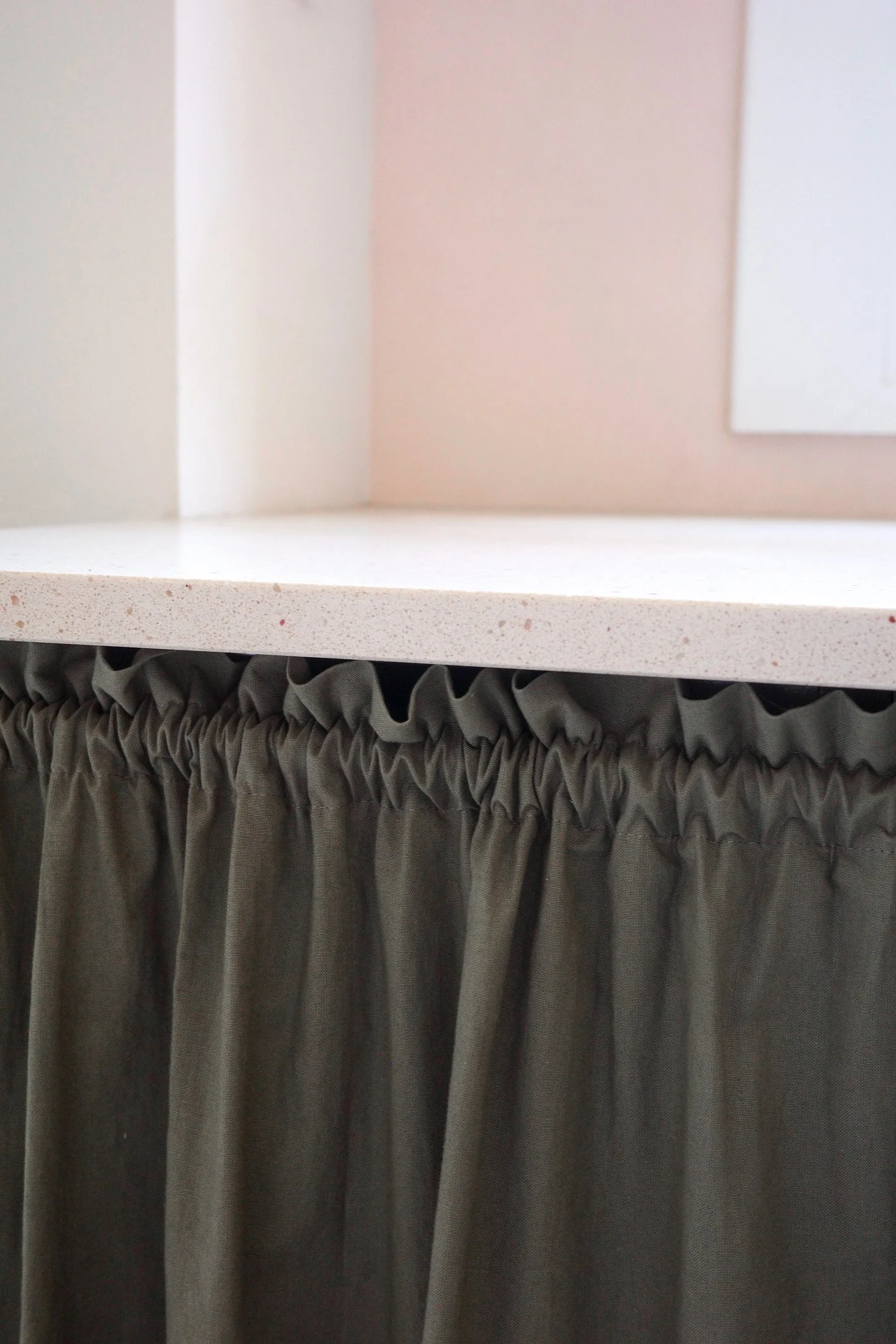 Close-up of a white shelf above a dark green curtain with a ruffled top.