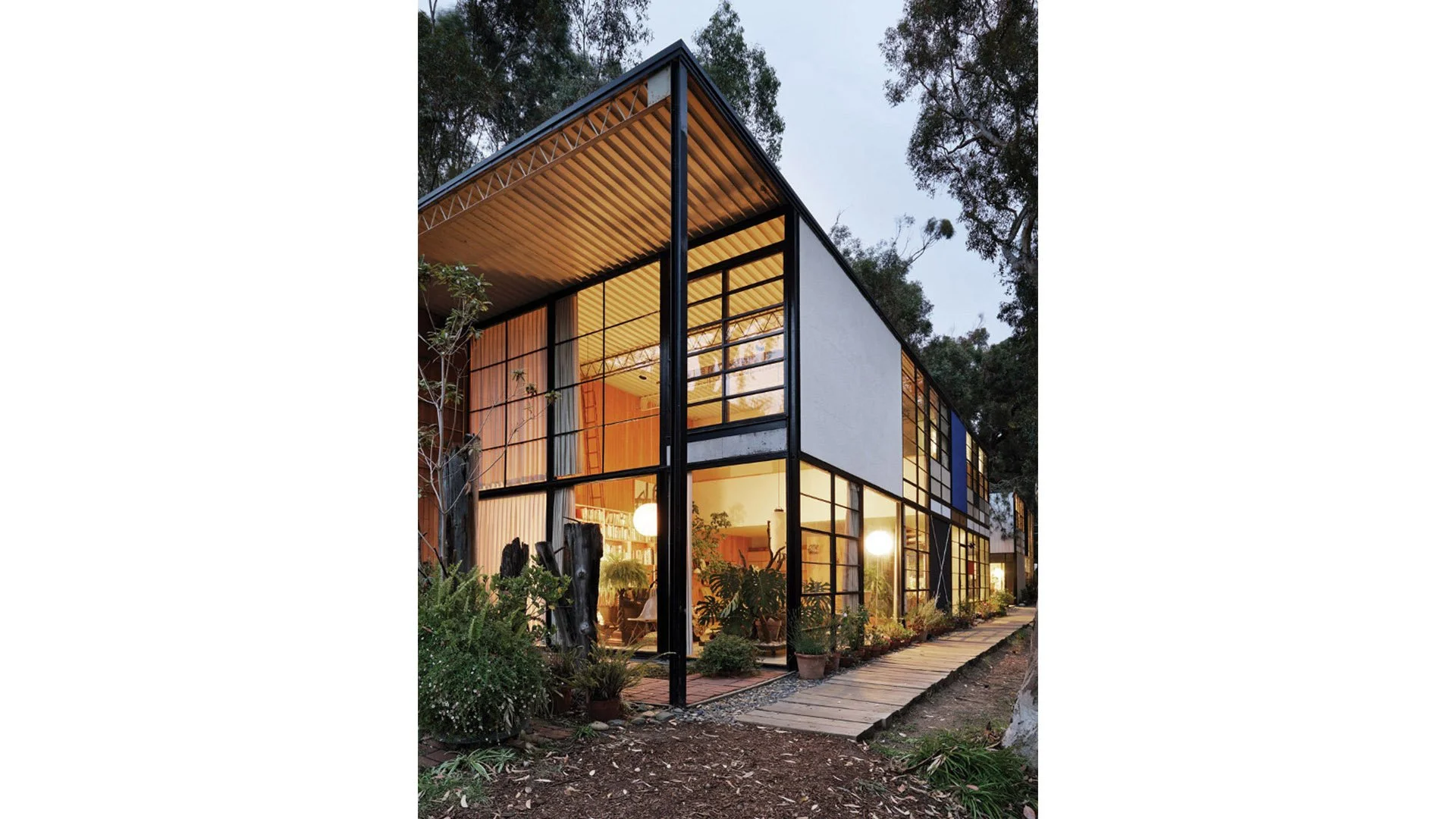 Modern multi-story house with large glass windows and a landscaped garden outside, at dusk.