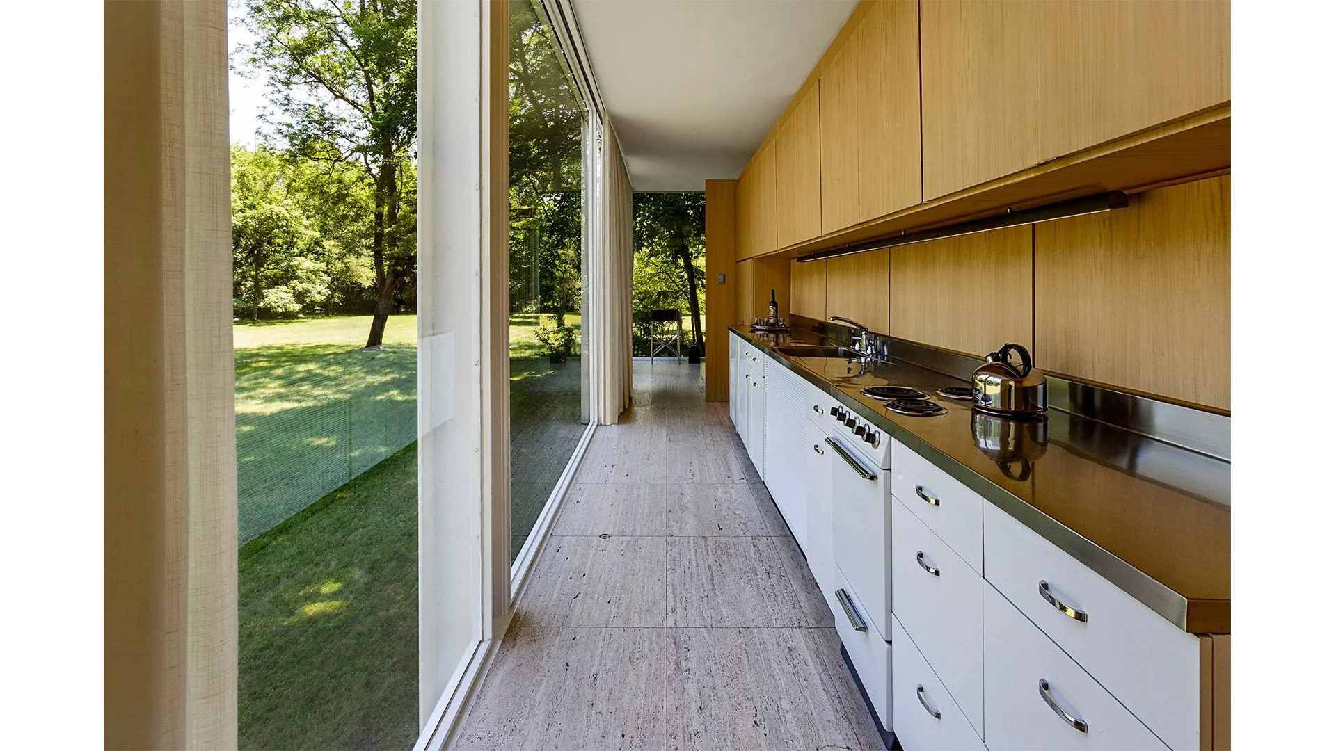 Kitchen with wood cabinets, white drawers, stove, kettle, sink, and large sliding glass door opening to a green backyard.
