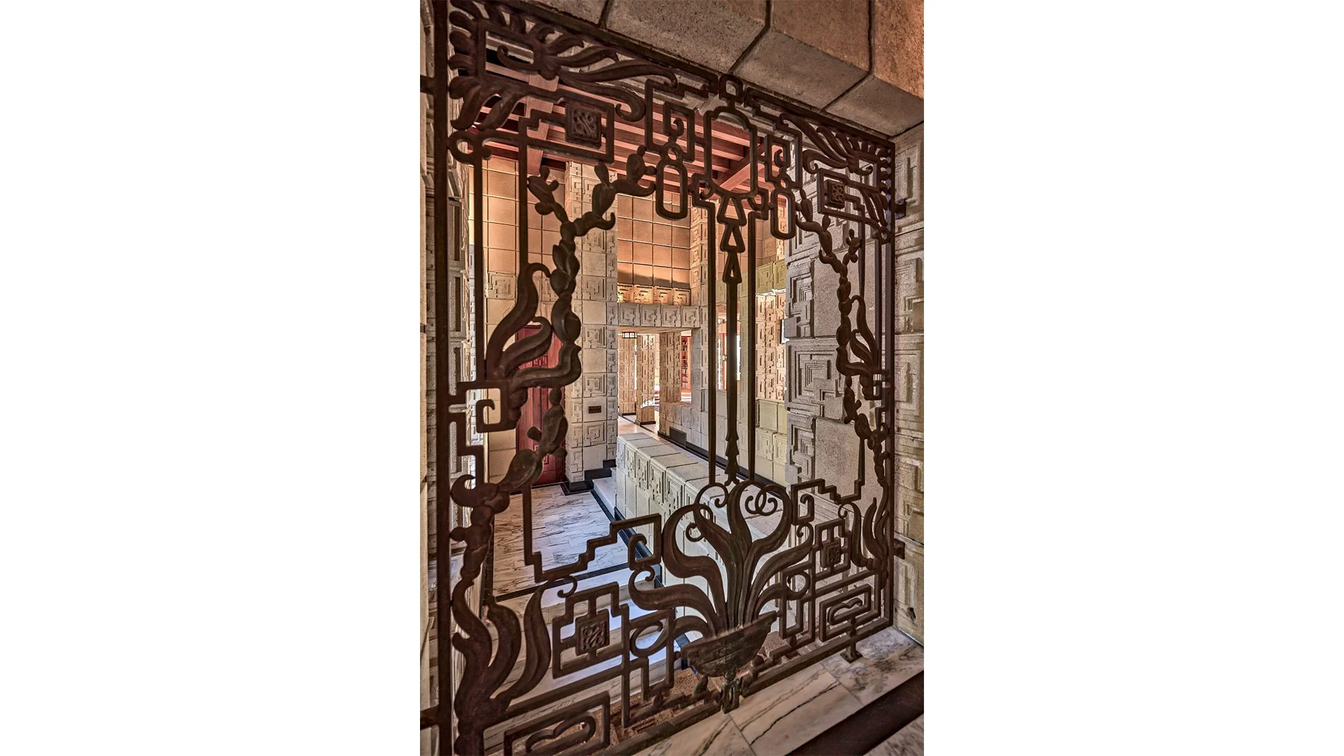 A decorative metal grille with intricate patterns, framing a view of a contemporary interior corridor with stone walls and a marble floor.