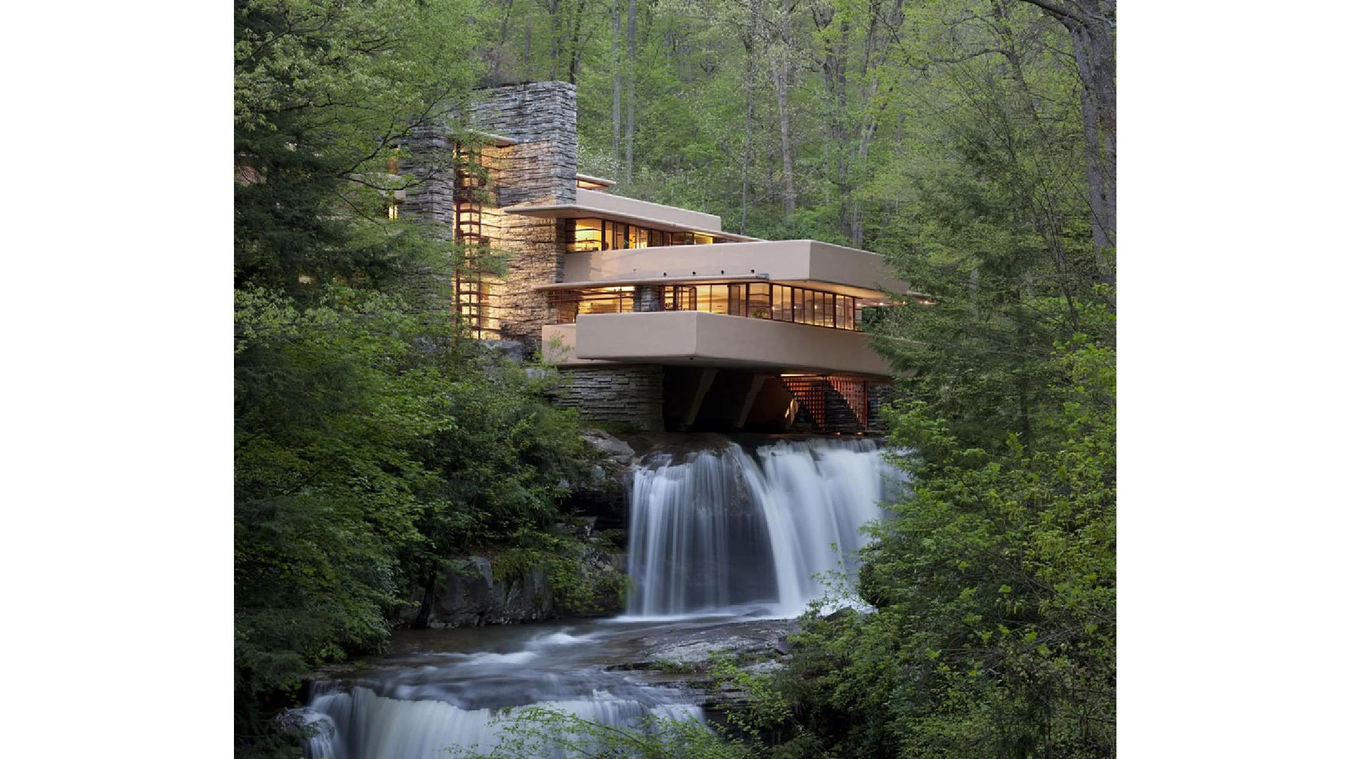 Modern house built on rocks and waterfall in a lush forest of green trees.
