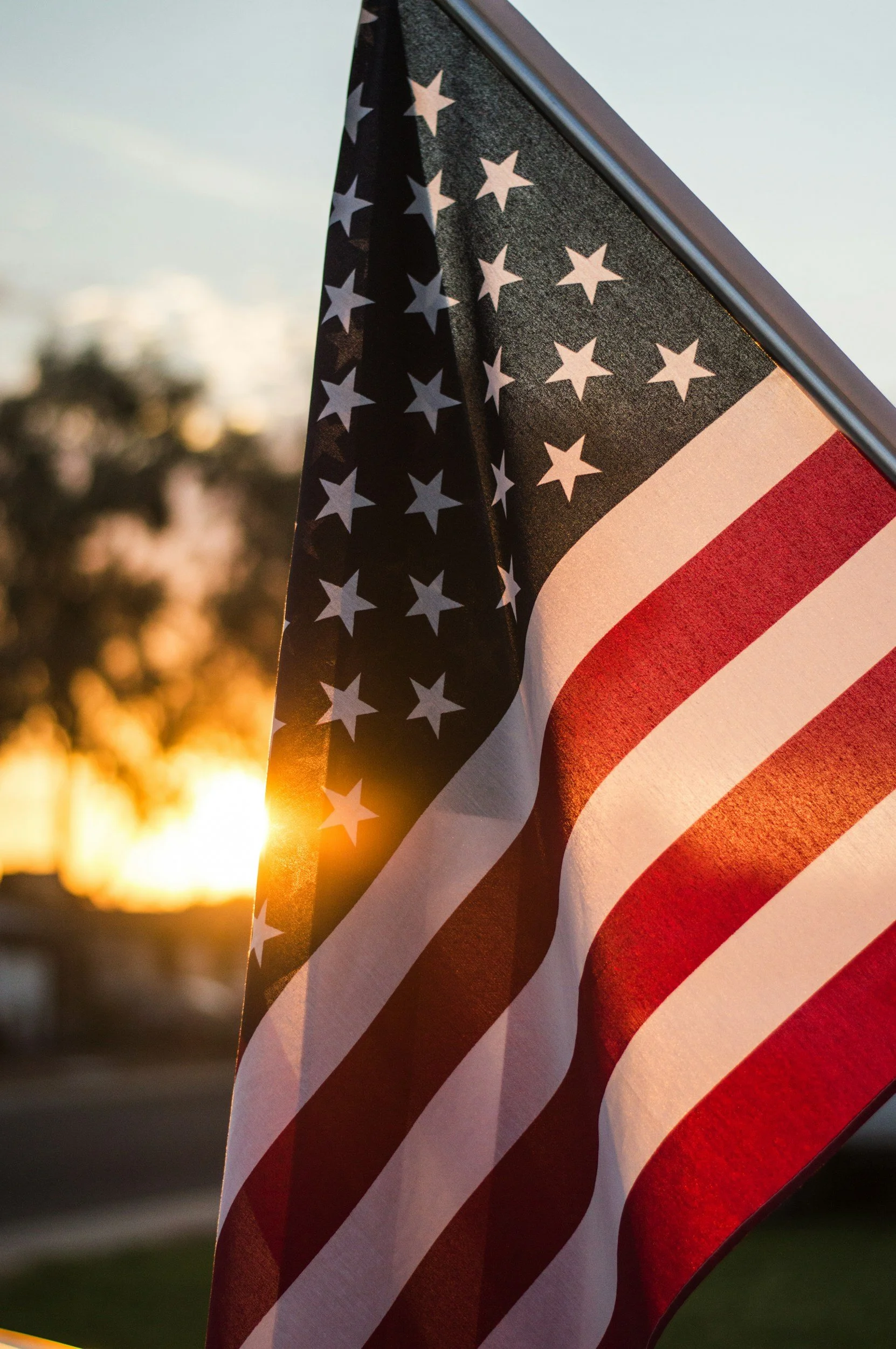 Close-up of American flag waving at sunset with trees in the background.